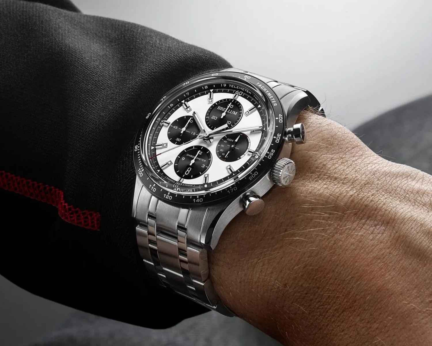Stainless steel chronograph wristwatch with black and white dial and tachymeter bezel worn on a wrist.