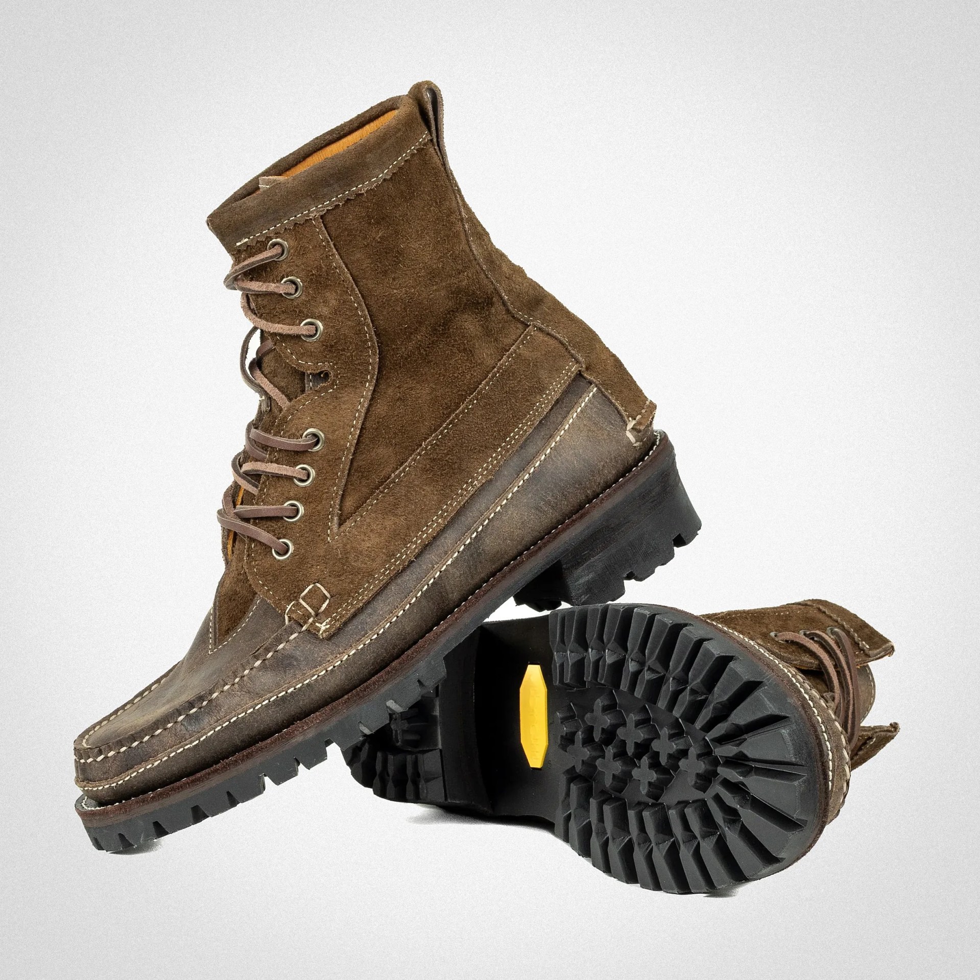 Pair of brown suede and leather lace-up boots with rugged black rubber soles, one boot showing tread pattern.