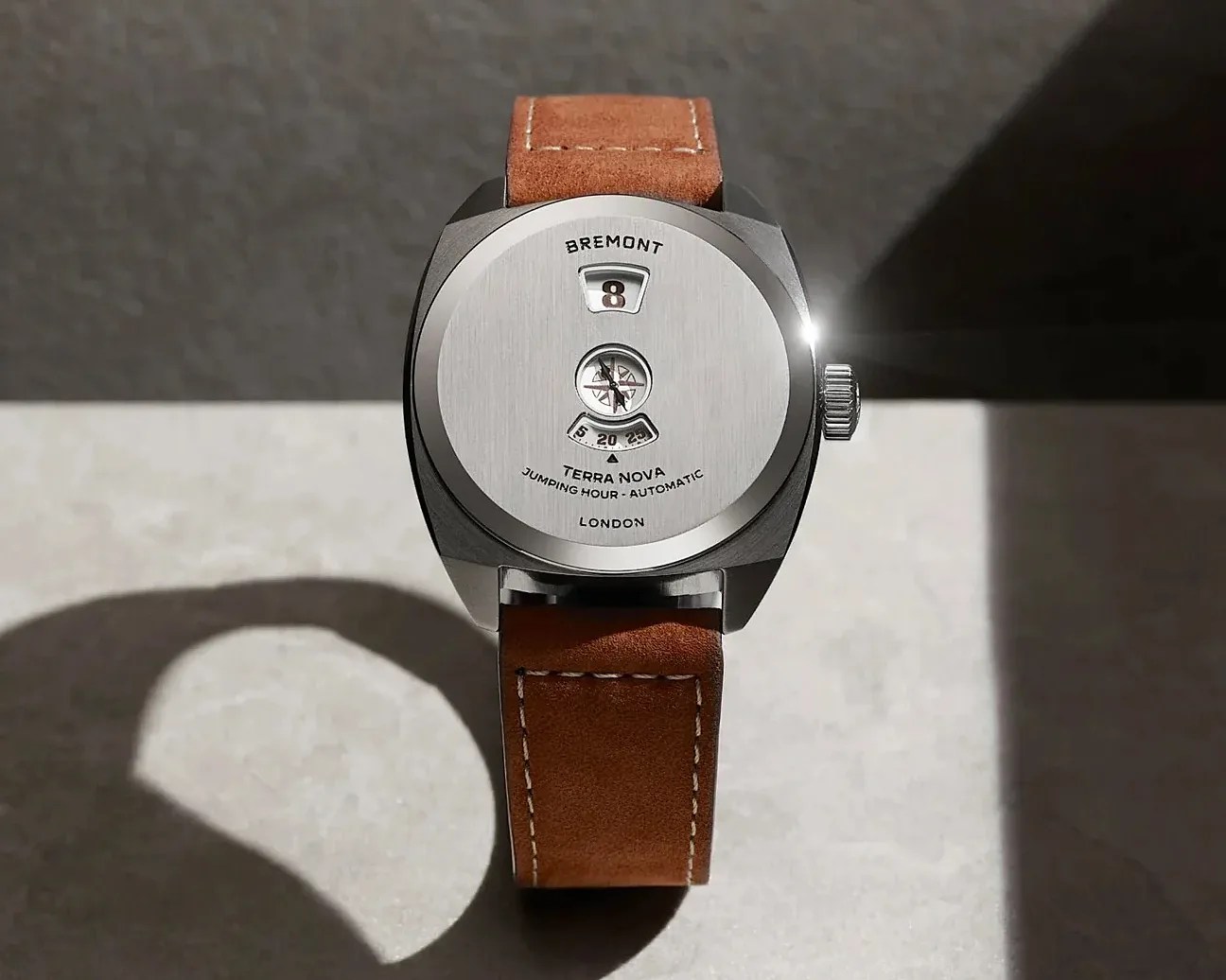 Silver Bremont Terra Nova watch with digital hour display and brown leather strap on a light surface.