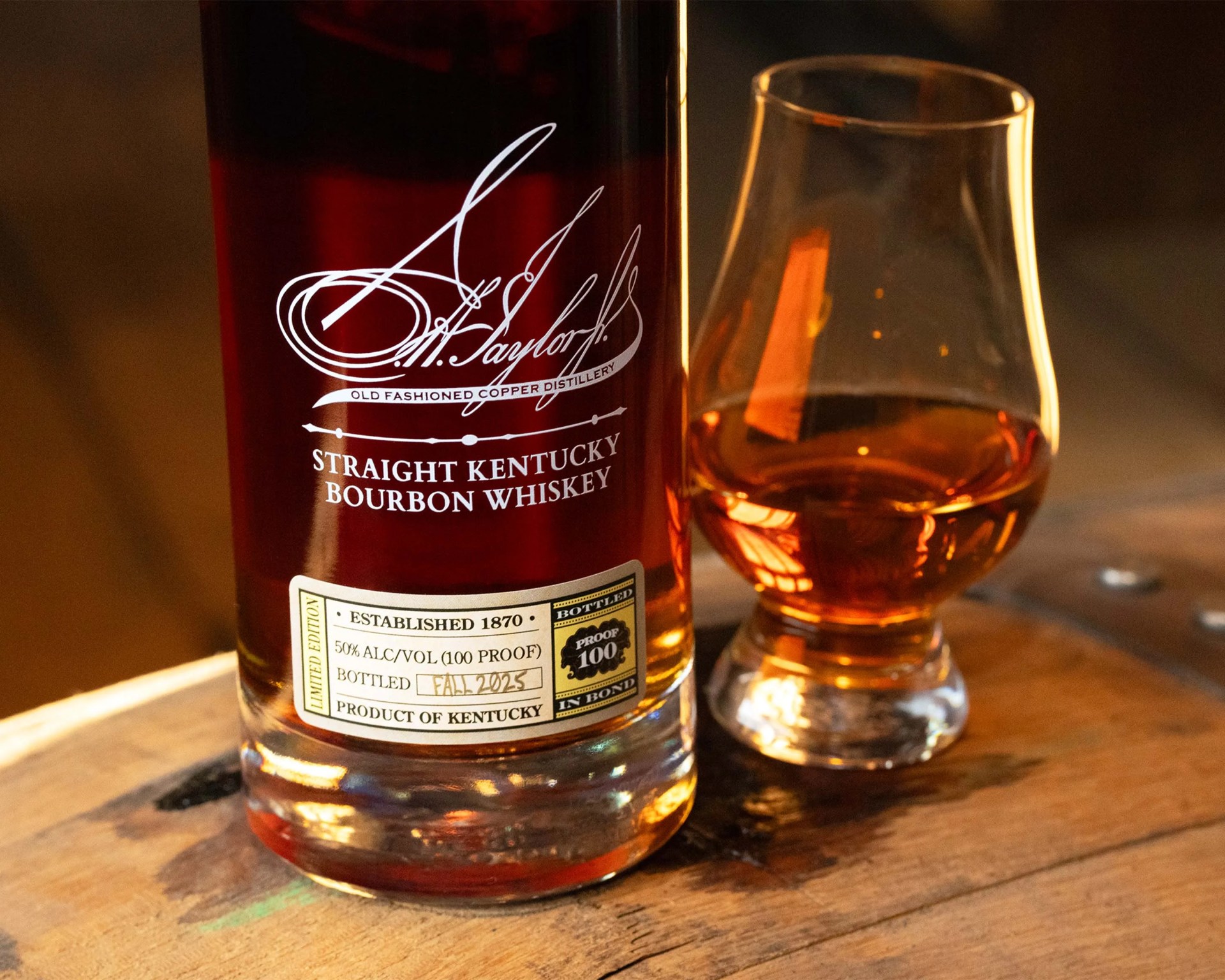 Bottle of A. Taylor Straight Kentucky Bourbon Whiskey with amber liquid in a glass on a wooden surface.