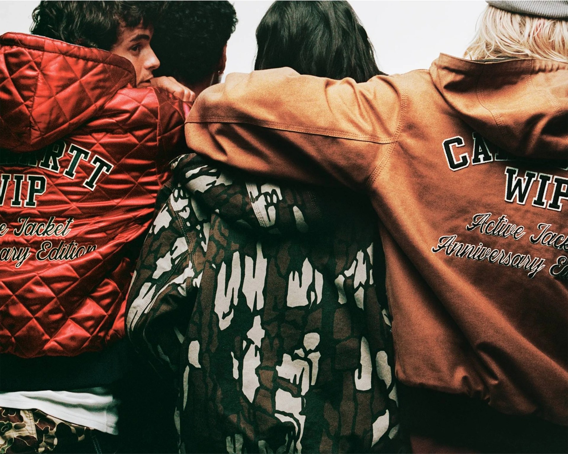 Group of four people wearing hooded jackets with visible text "CARHARTT WIP Active Jacket Anniversary Edition" on two jackets.