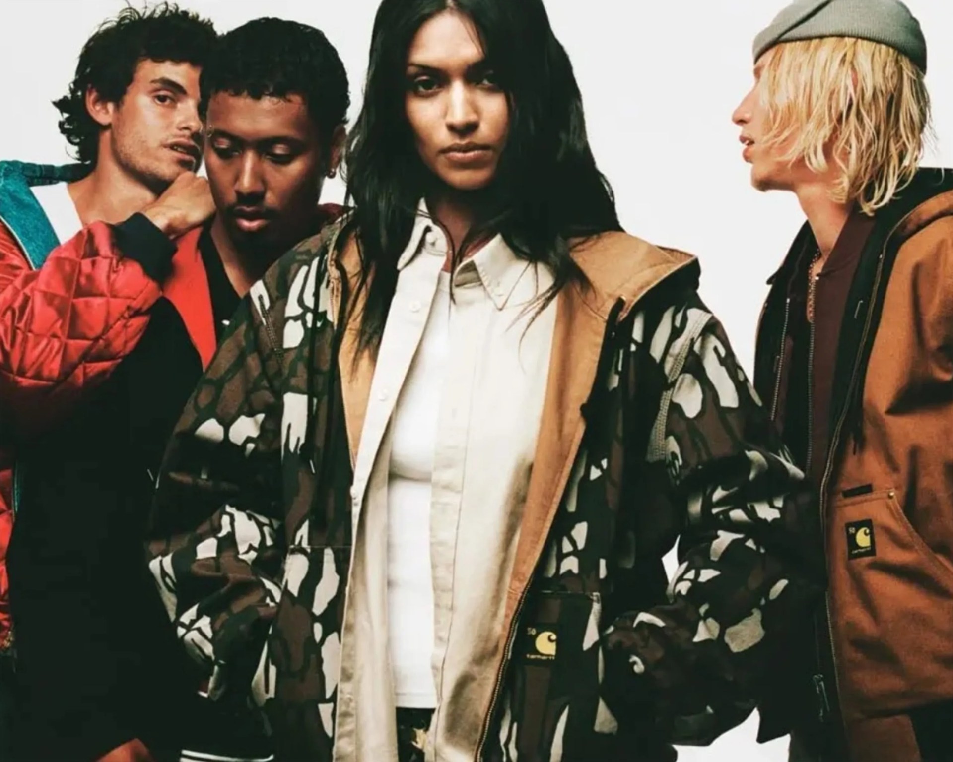 Group of four people wearing various jackets, including a camouflage and tan Carhartt jacket in the center.