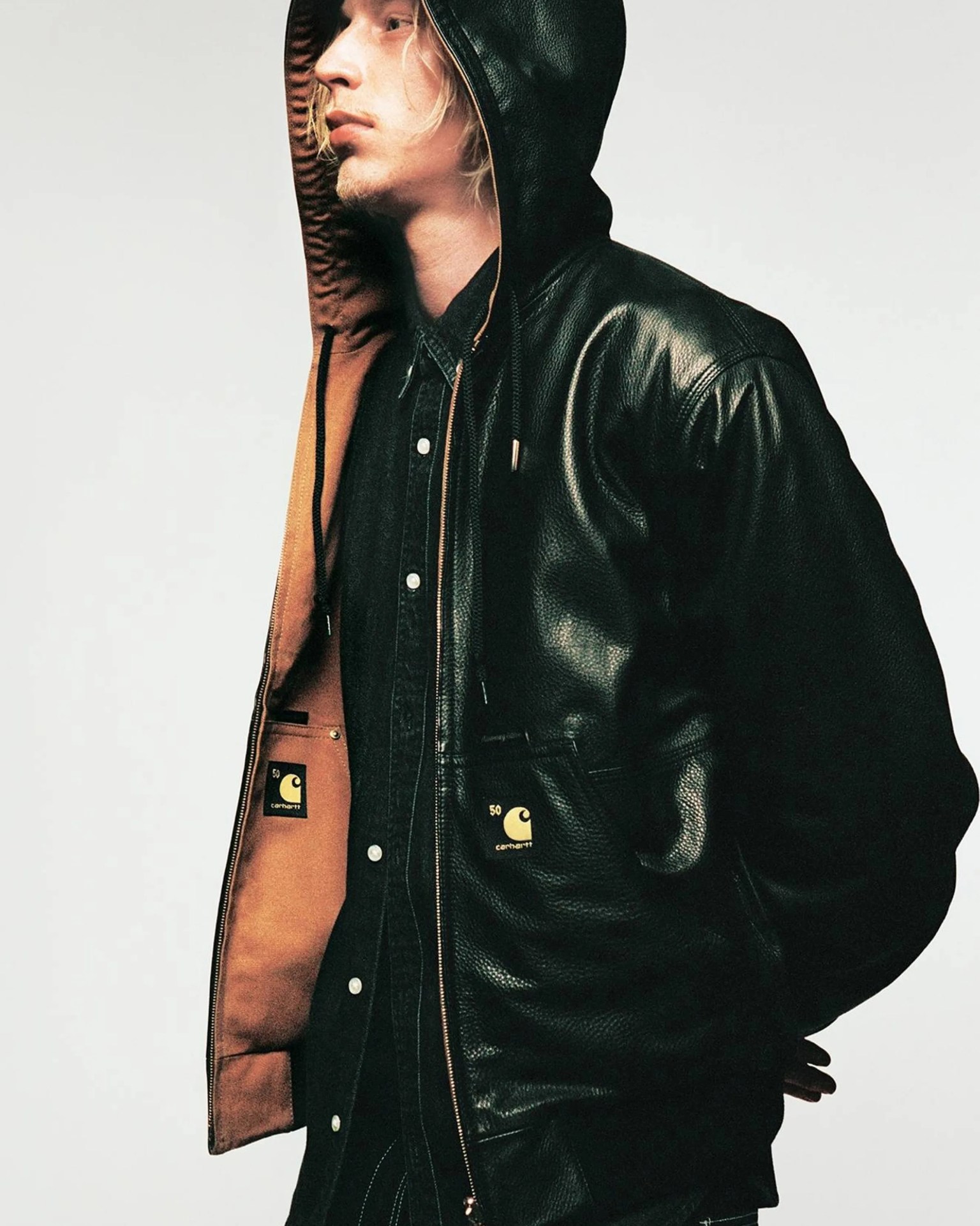 Black leather Carhartt hooded jacket with brown interior lining worn over a black button-up shirt.