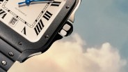 Close-up of a square silver watch with black screws, white dial, blue hands, and Roman numerals against a sky background.