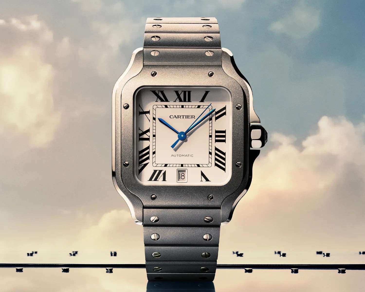 Square silver Cartier wristwatch with blue hands, black Roman numerals, and metal bracelet against a cloudy sky background.