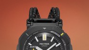 Close-up of the top half of a black Casio Pro Trek watch with a black and white braided strap against an orange background.