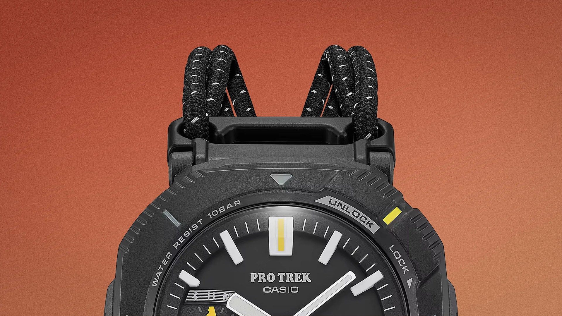 Close-up of the top half of a black Casio Pro Trek watch with a black and white braided strap against an orange background.