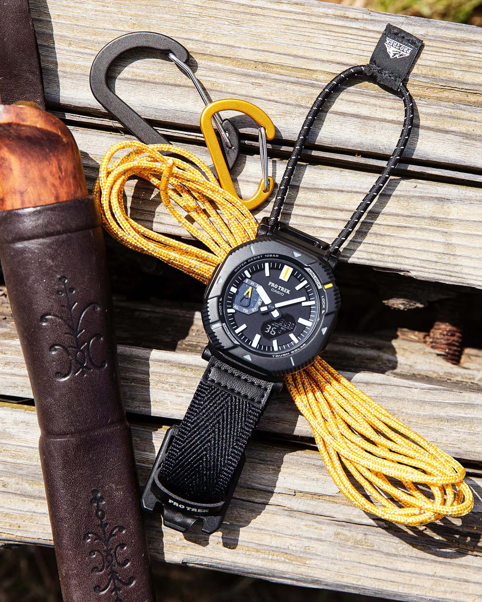 Black Casio Pro Trek watch with fabric strap, yellow paracord, and two carabiners on wooden surface.