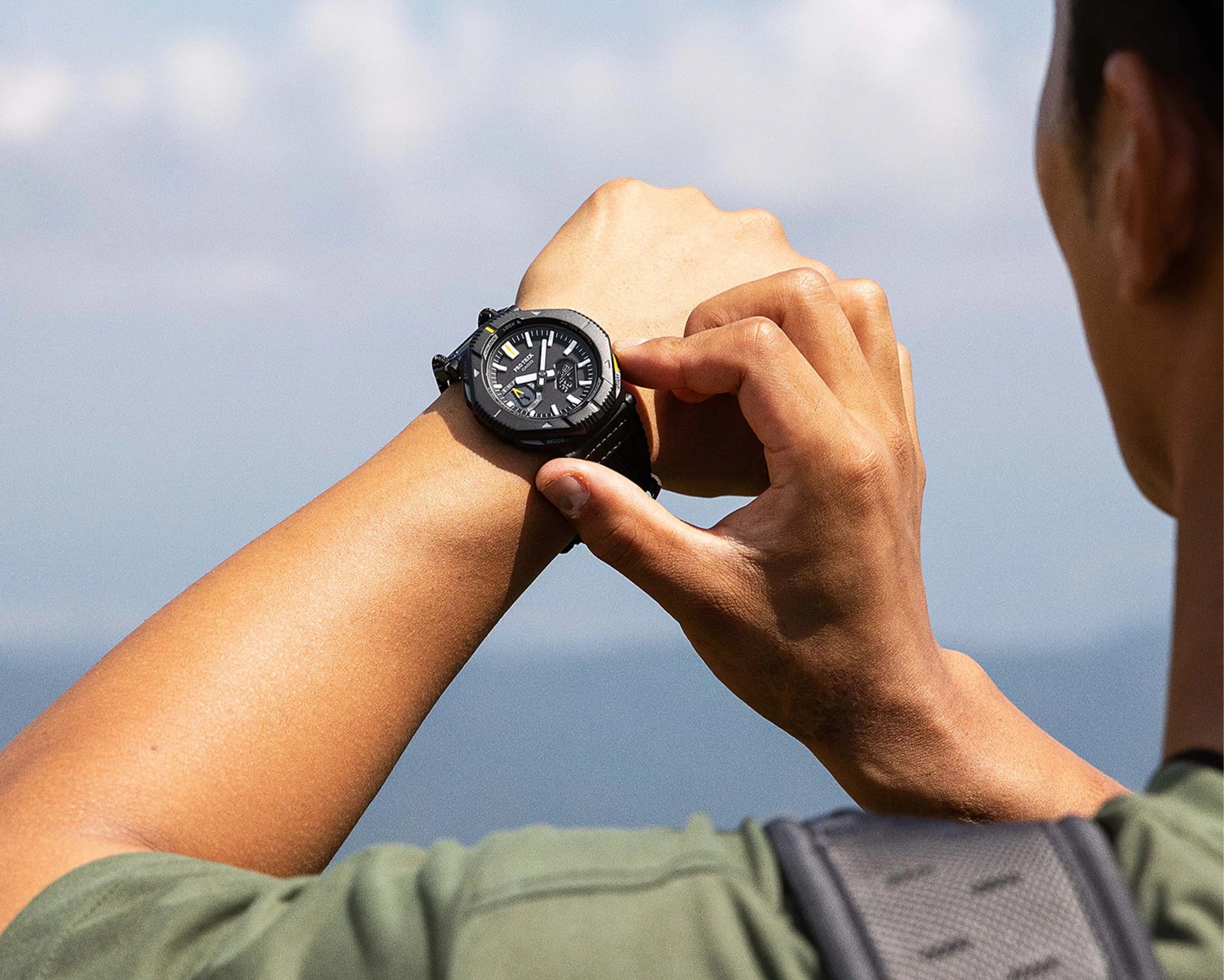 Black digital-analog wristwatch with a round face and yellow accents worn on a wrist outdoors.