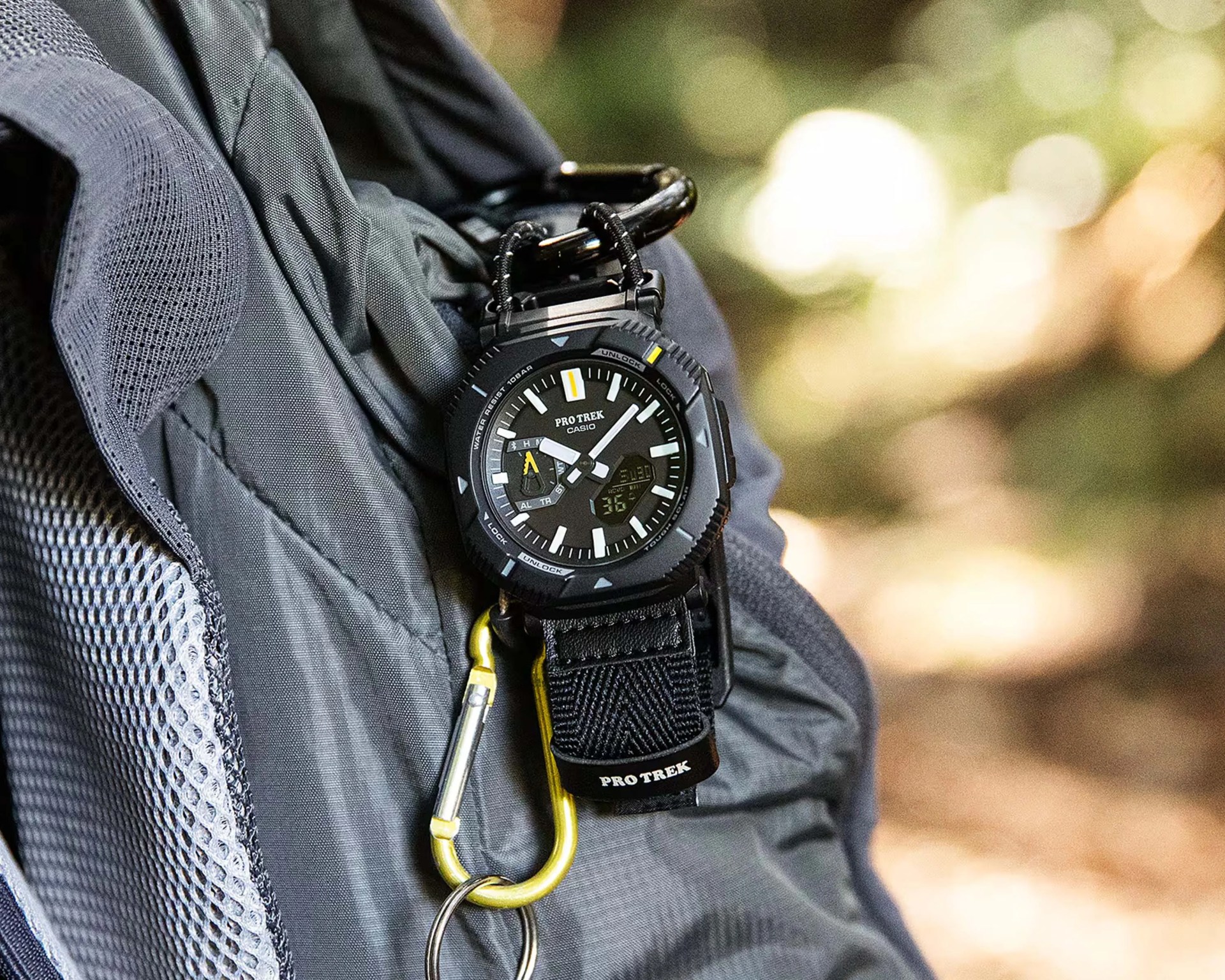 Black Casio Pro Trek watch with analog-digital display attached to a gray backpack with a yellow carabiner.