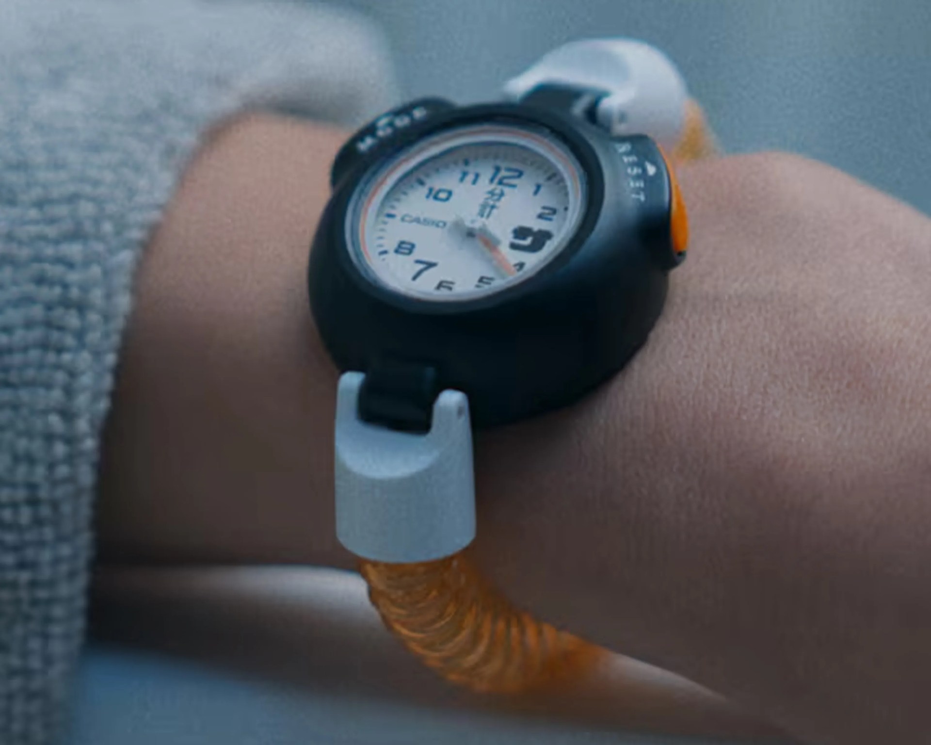 Black Casio wristwatch with white dial and orange translucent strap worn on a wrist.