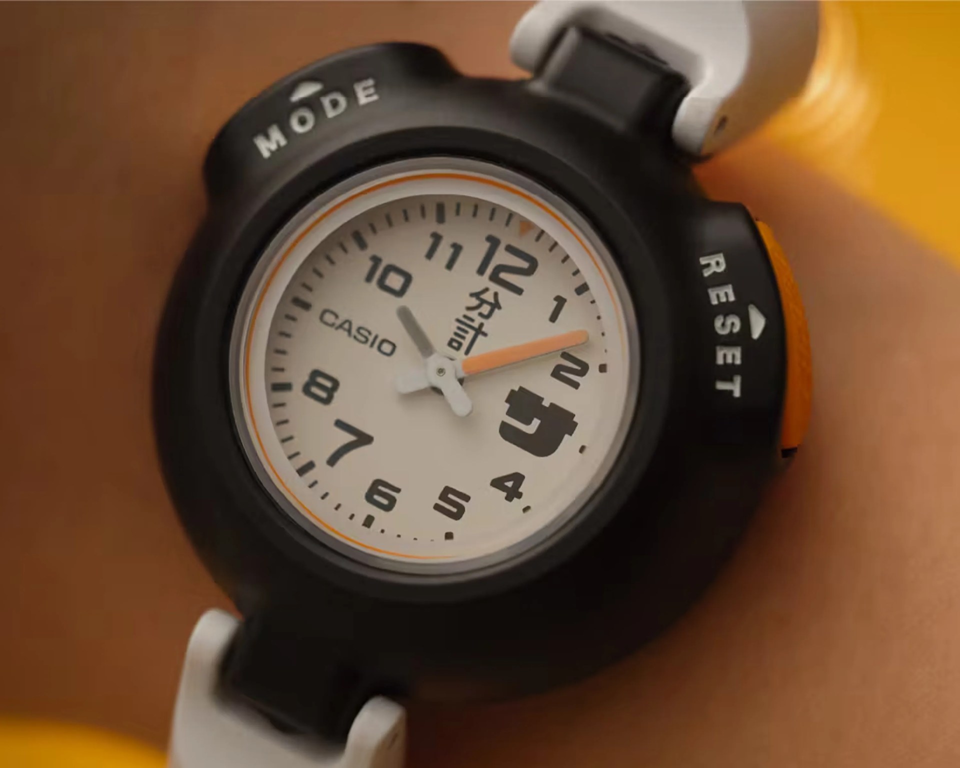 Black Casio stopwatch with white dial, orange second hand, and white strap on a wrist.