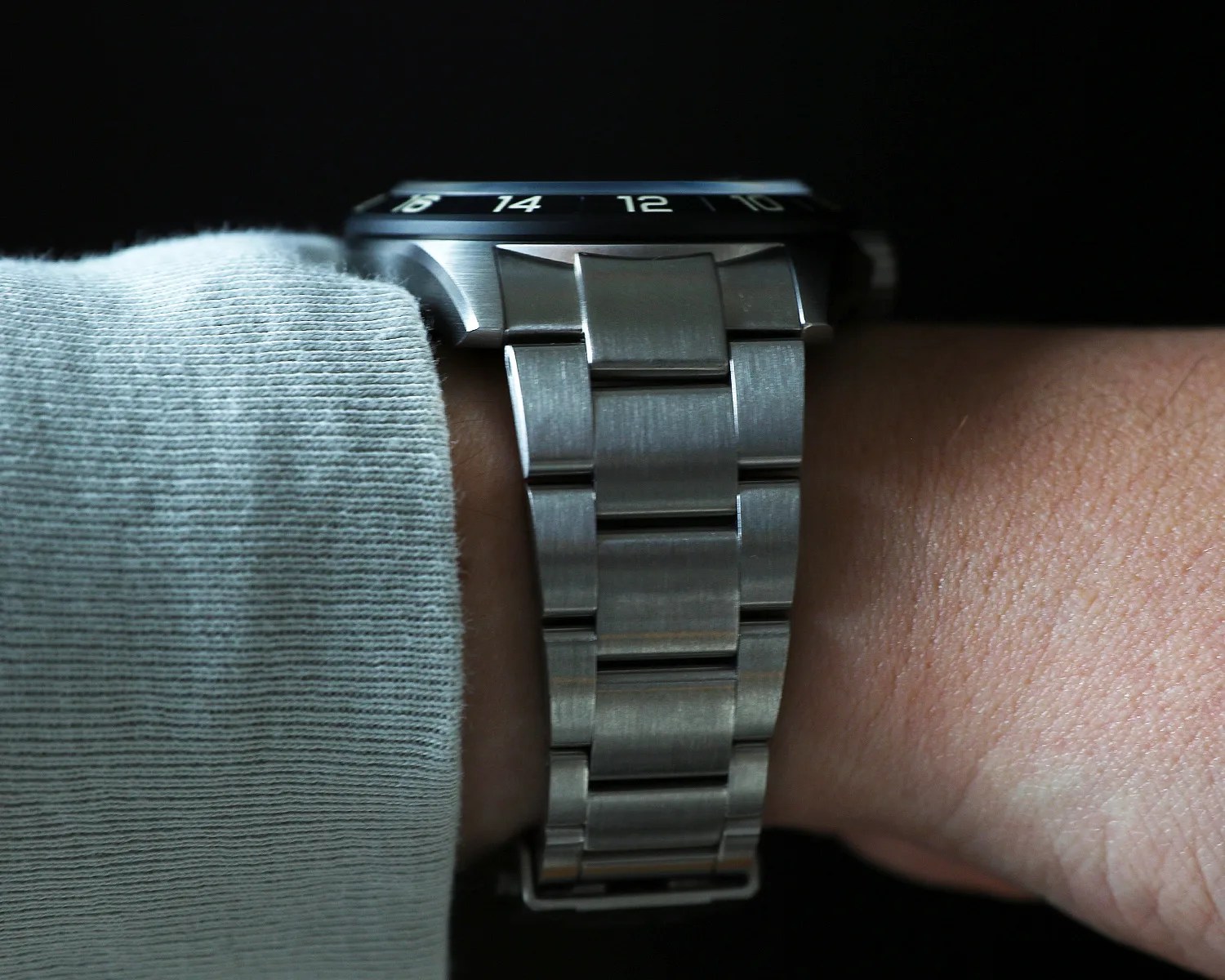 Brushed stainless steel watch band with a black bezel showing numbers on a wrist.