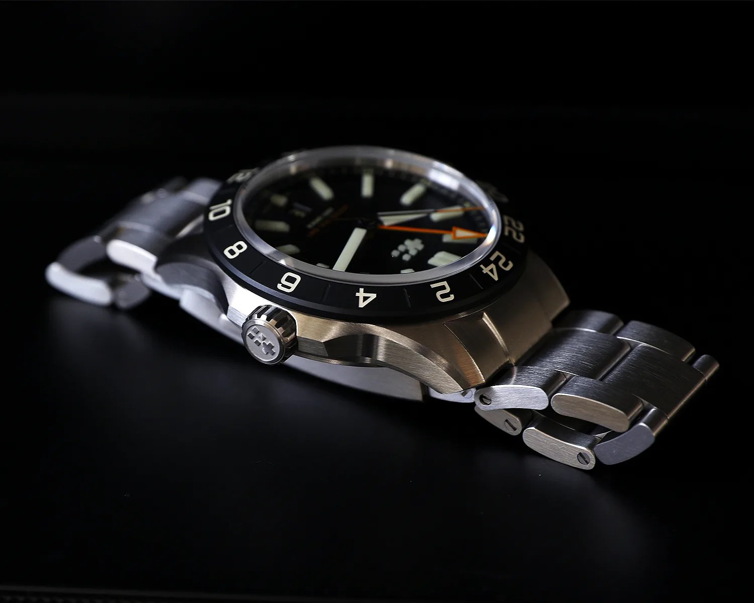 Stainless steel wristwatch with black bezel and orange-tipped hands on a black surface.