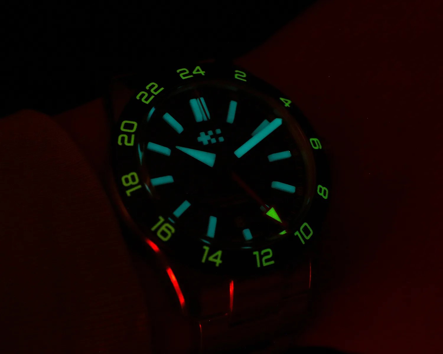 Wristwatch with glowing blue hour markers and green 24-hour bezel numbers in low light.