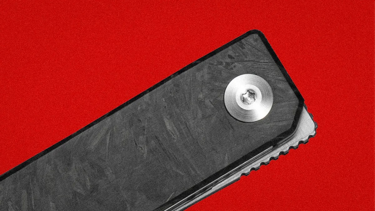 Close-up of a black textured folding knife handle with a silver screw on a red background.
