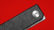 Close-up of a black textured folding knife handle with a silver screw on a red background.