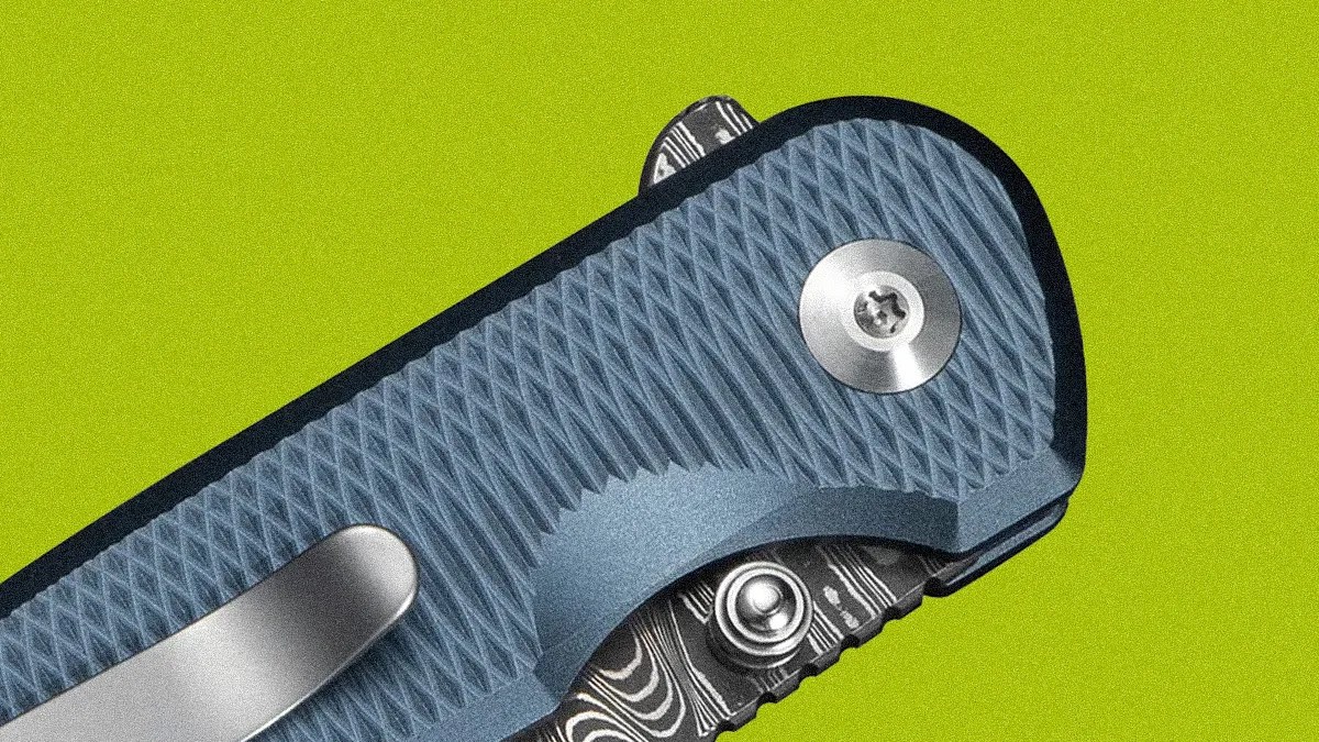 Close-up of a blue textured folding knife handle with a metal clip and patterned blade.
