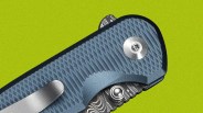 Close-up of a blue textured folding knife handle with a metal clip and patterned blade.