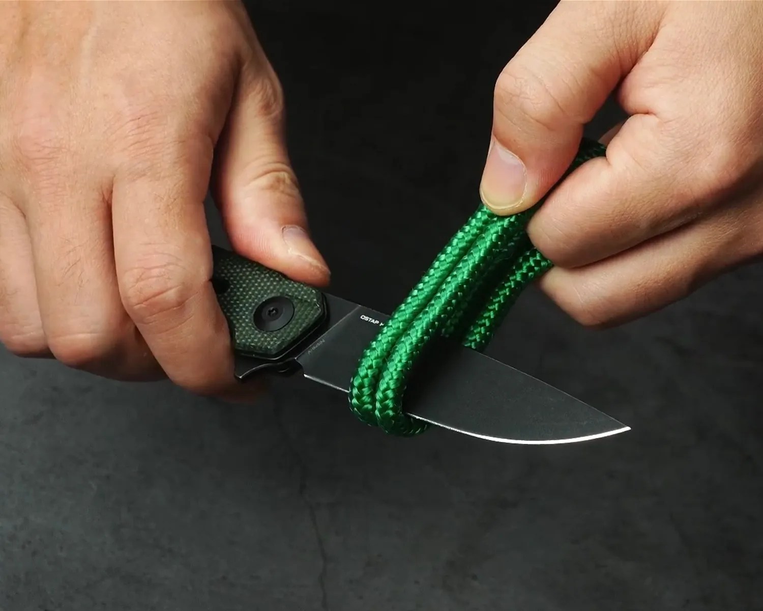 Hands holding a green-handled folding knife cutting through green braided rope.