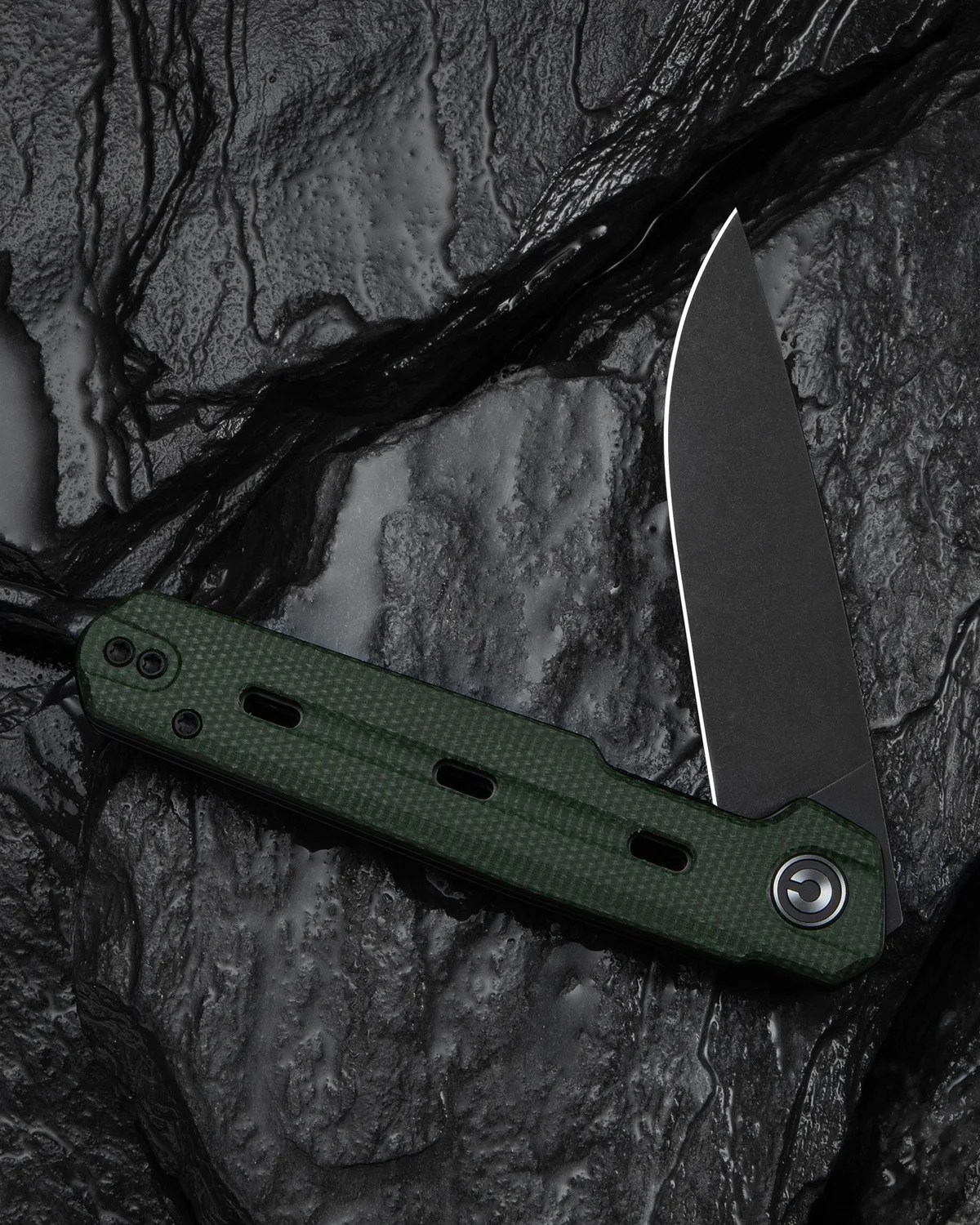 Folding knife with a black blade and textured dark green handle on a black textured surface.