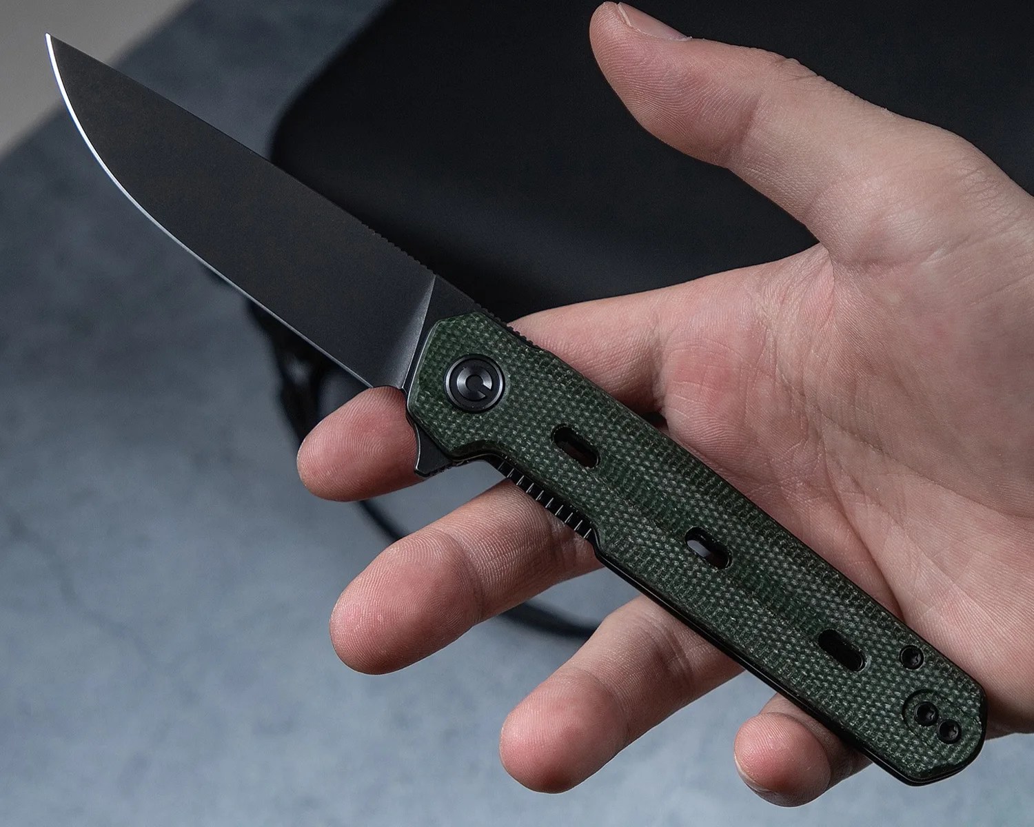 Hand holding a folding knife with a black blade and green textured handle.