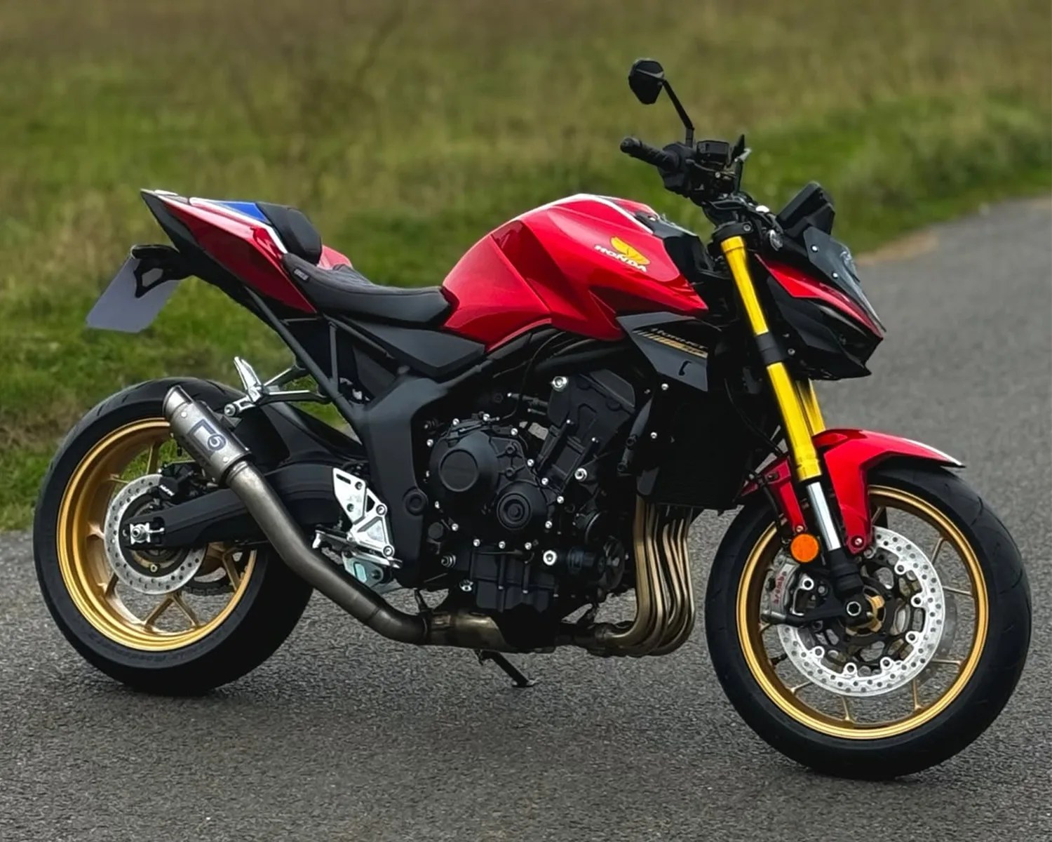 Red and black Honda motorcycle with gold wheels and yellow front forks parked on a road.