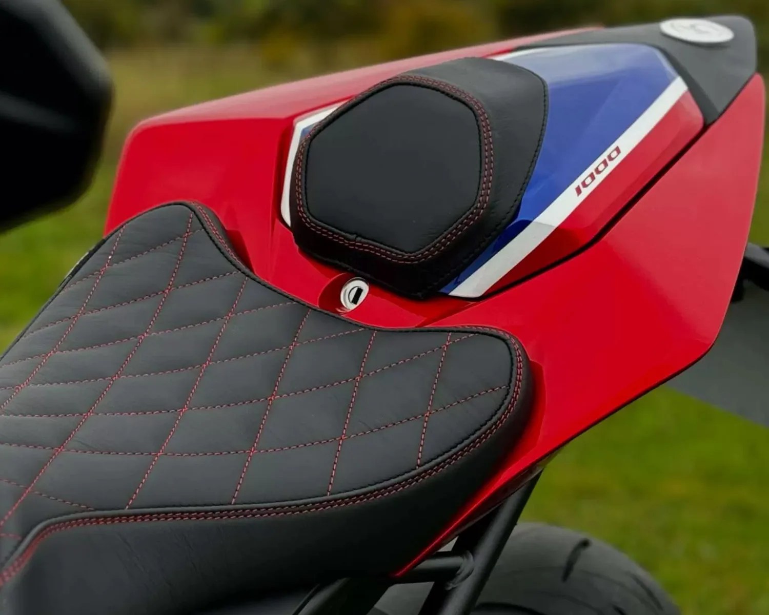 Black leather motorcycle seat with red stitching on a red bike tail section marked "1000" with blue and white accents.