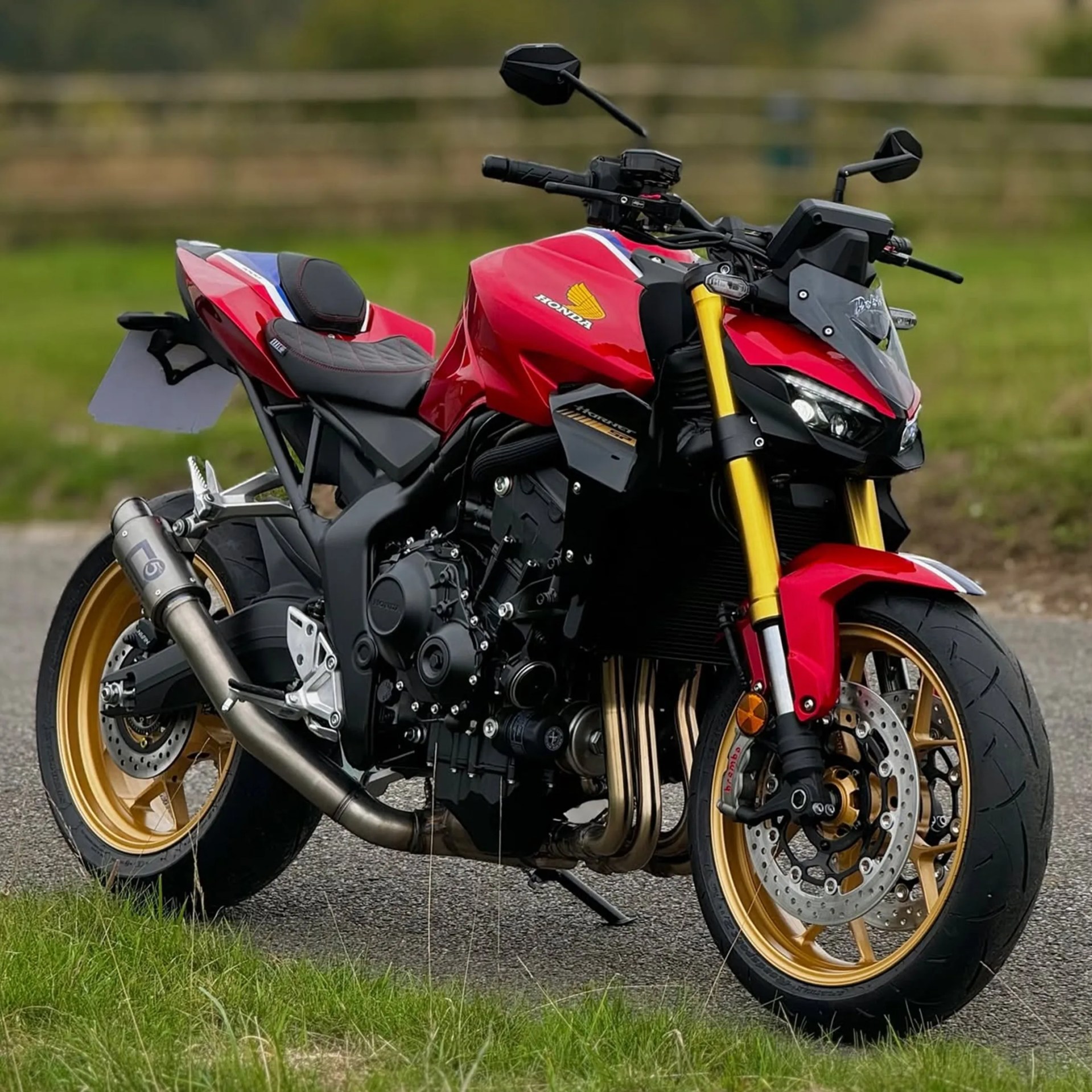 Red Honda motorcycle with gold wheels and front forks parked on a paved road beside grass.