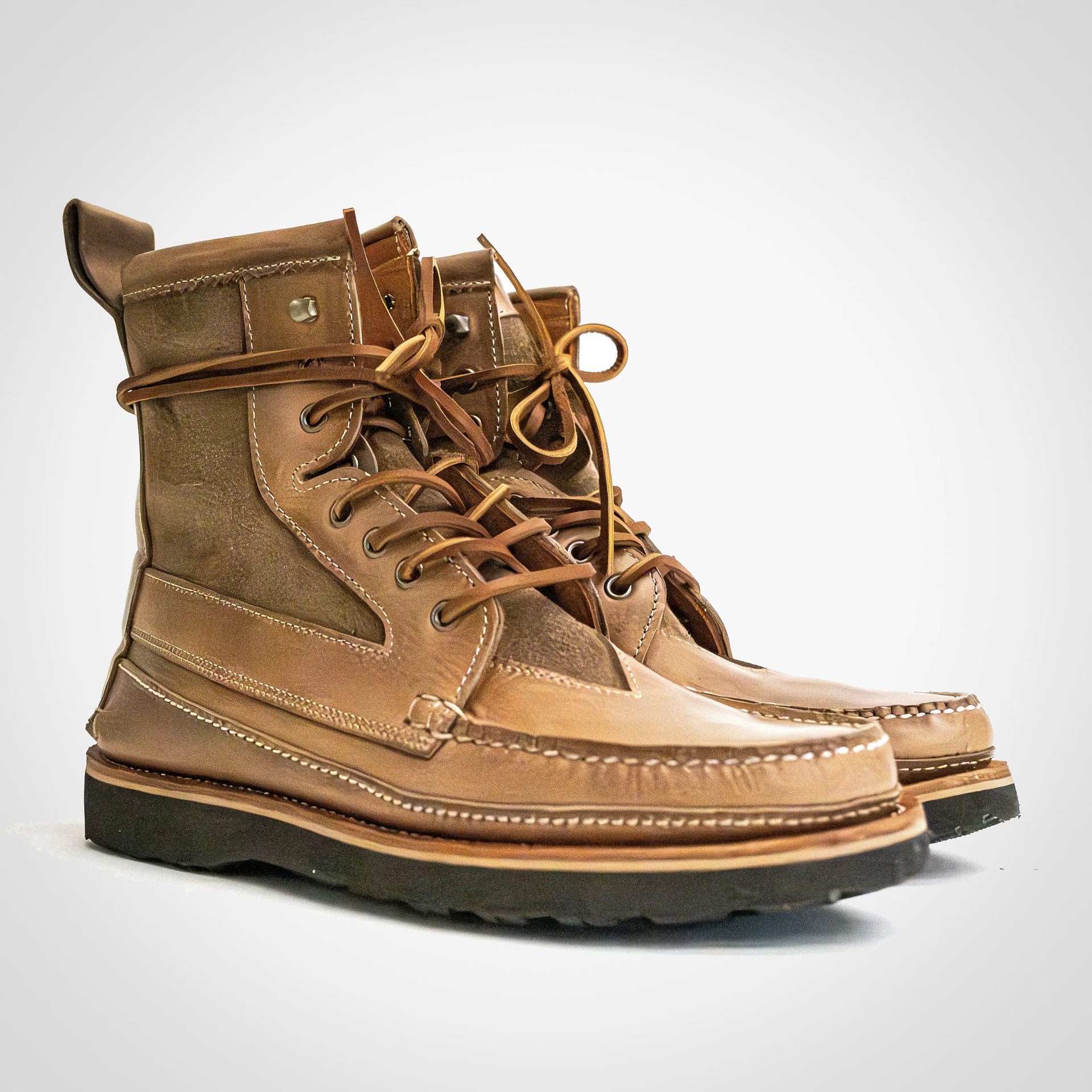 Pair of tan leather lace-up boots with black rubber soles on a white background.