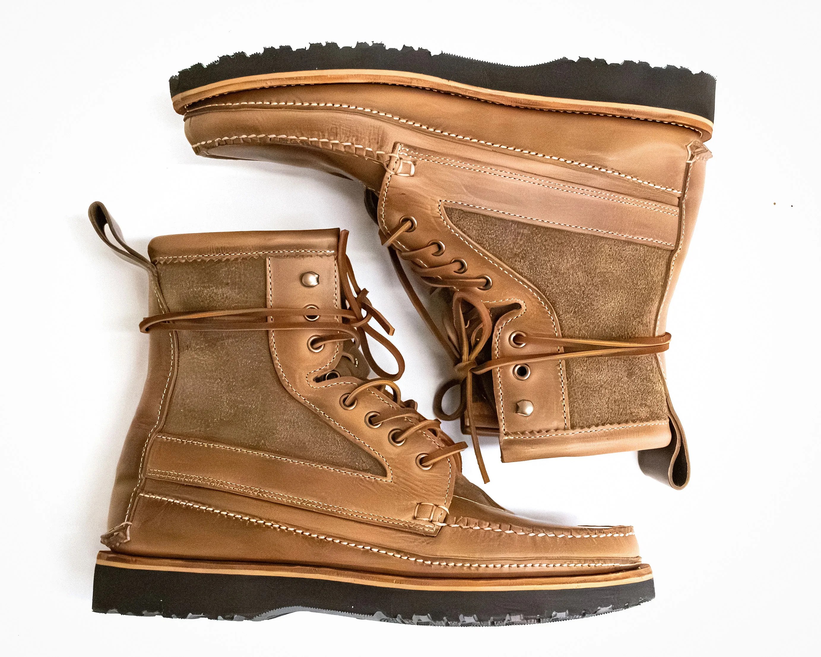 Pair of tan leather and suede lace-up boots with black rubber soles on a white background.