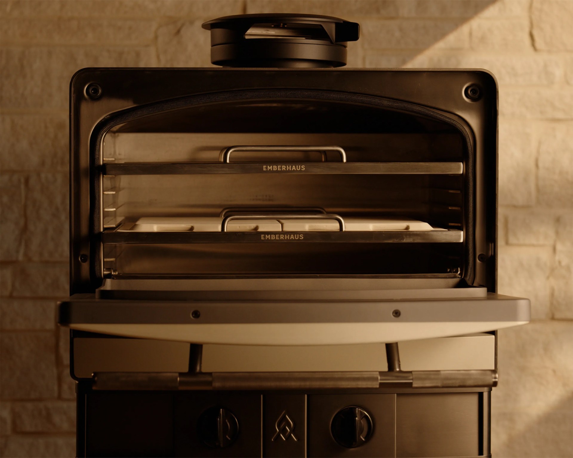 Black Emberhaus outdoor pizza oven with open door showing two metal racks and stone baking trays inside.