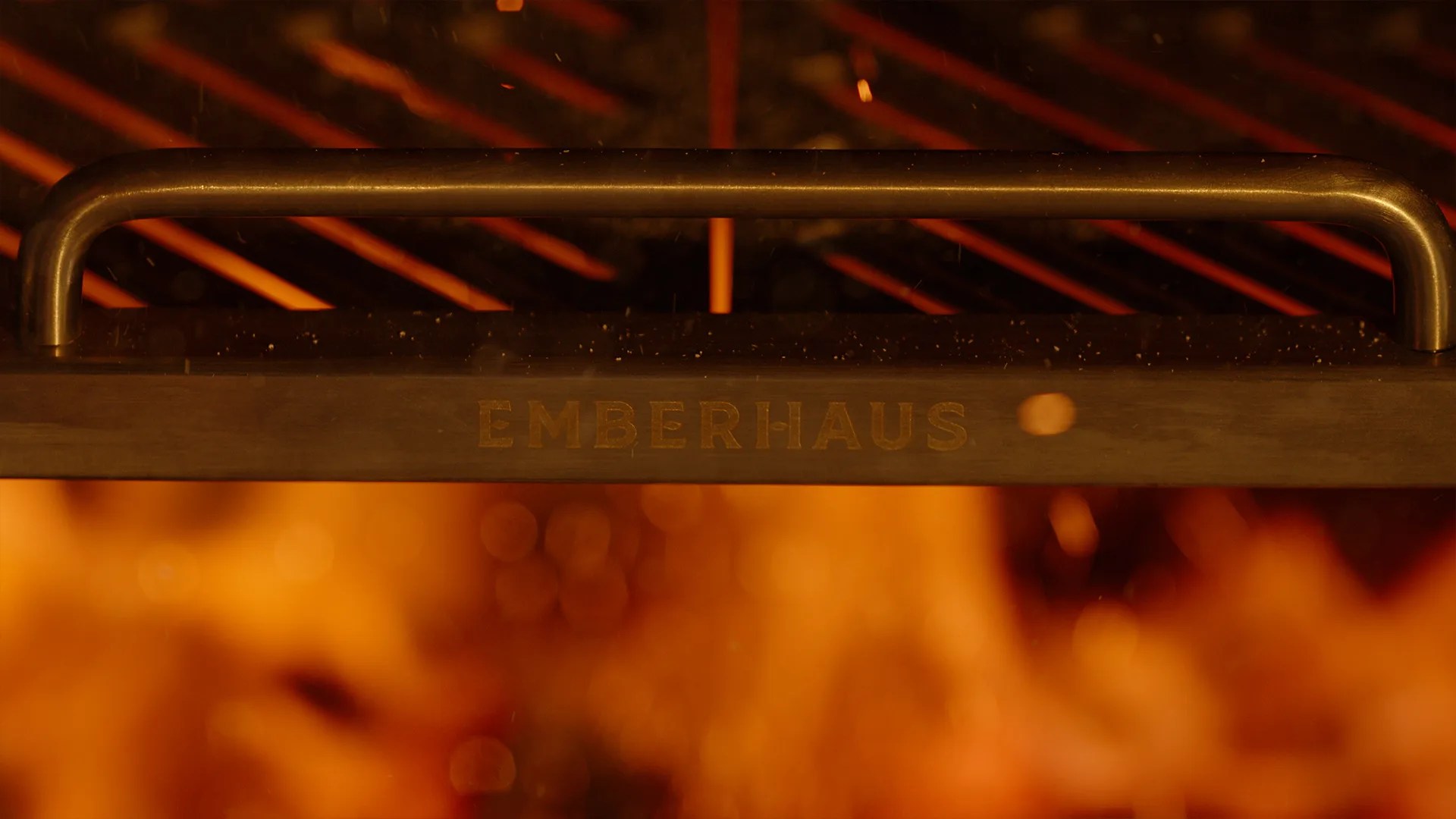 Black metal grill handle with the brand name "EMBERHAUS" visible against a background of glowing orange flames.