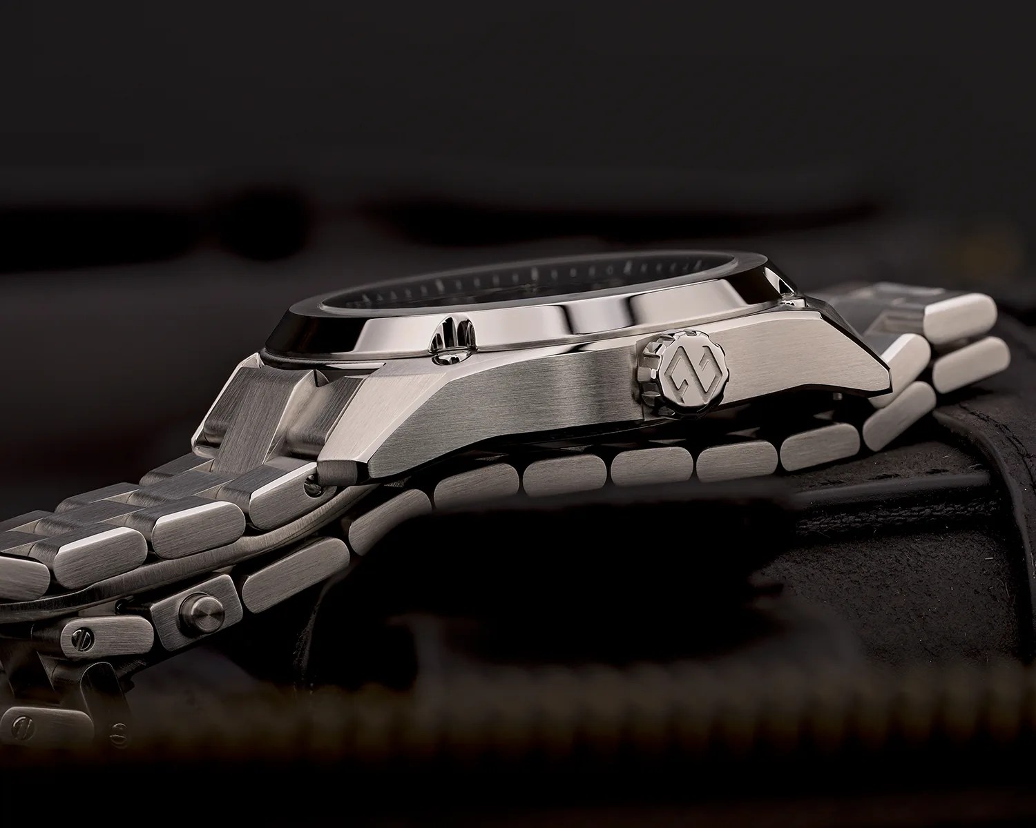 Side view of a stainless steel wristwatch with a brushed metal finish and a linked bracelet on a dark surface.