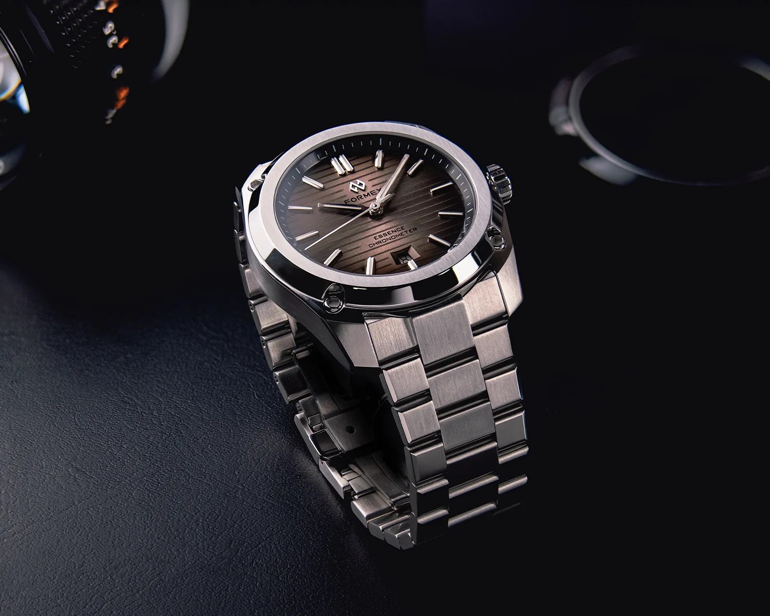 Stainless steel wristwatch with a brown textured dial and metal link bracelet on a dark surface.