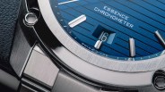 Close-up of a stainless steel watch with a blue dial showing "ESSENCE CHRONOMETER" and a date window displaying "16".