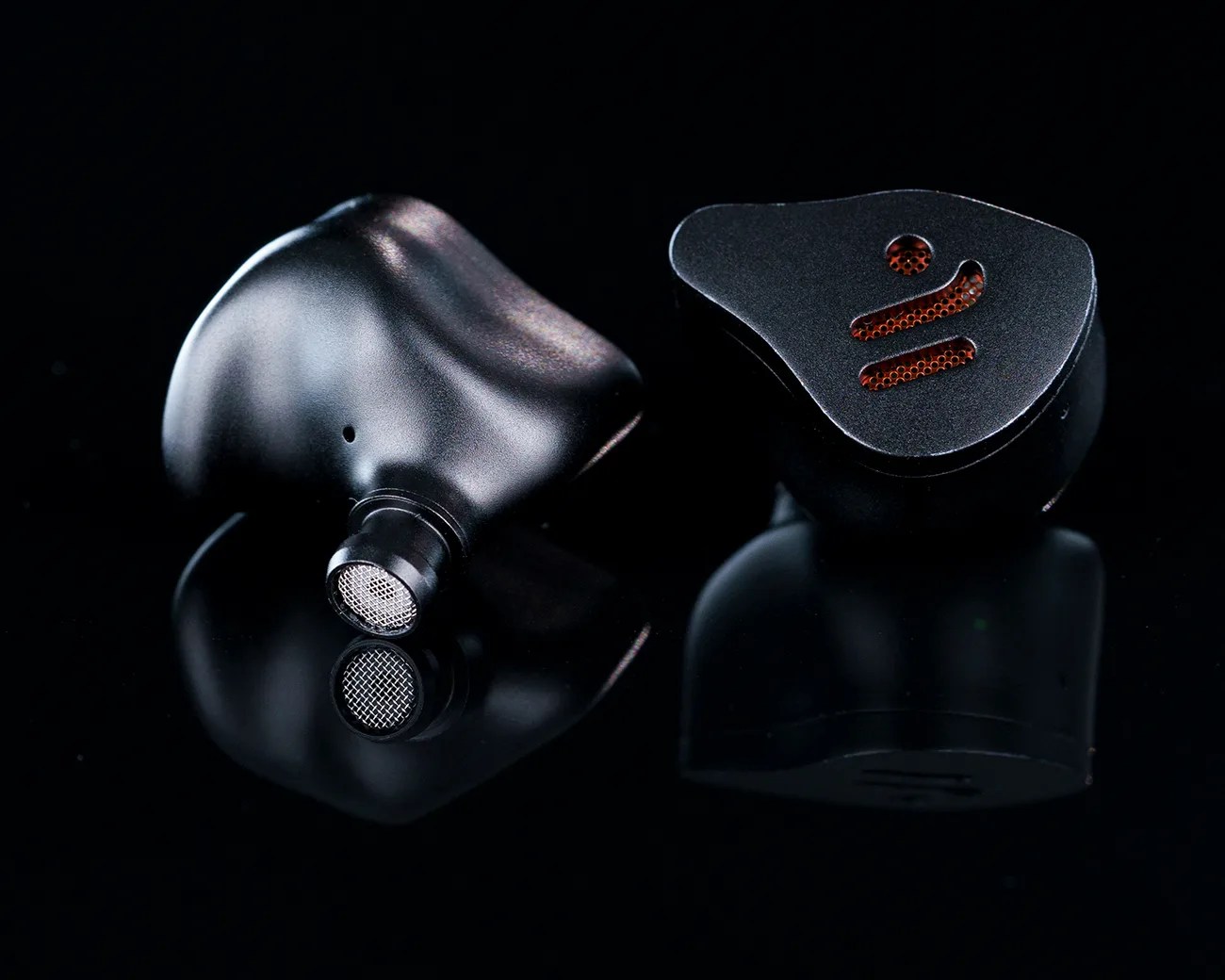 Pair of black in-ear monitors with red mesh accents on a reflective black surface.