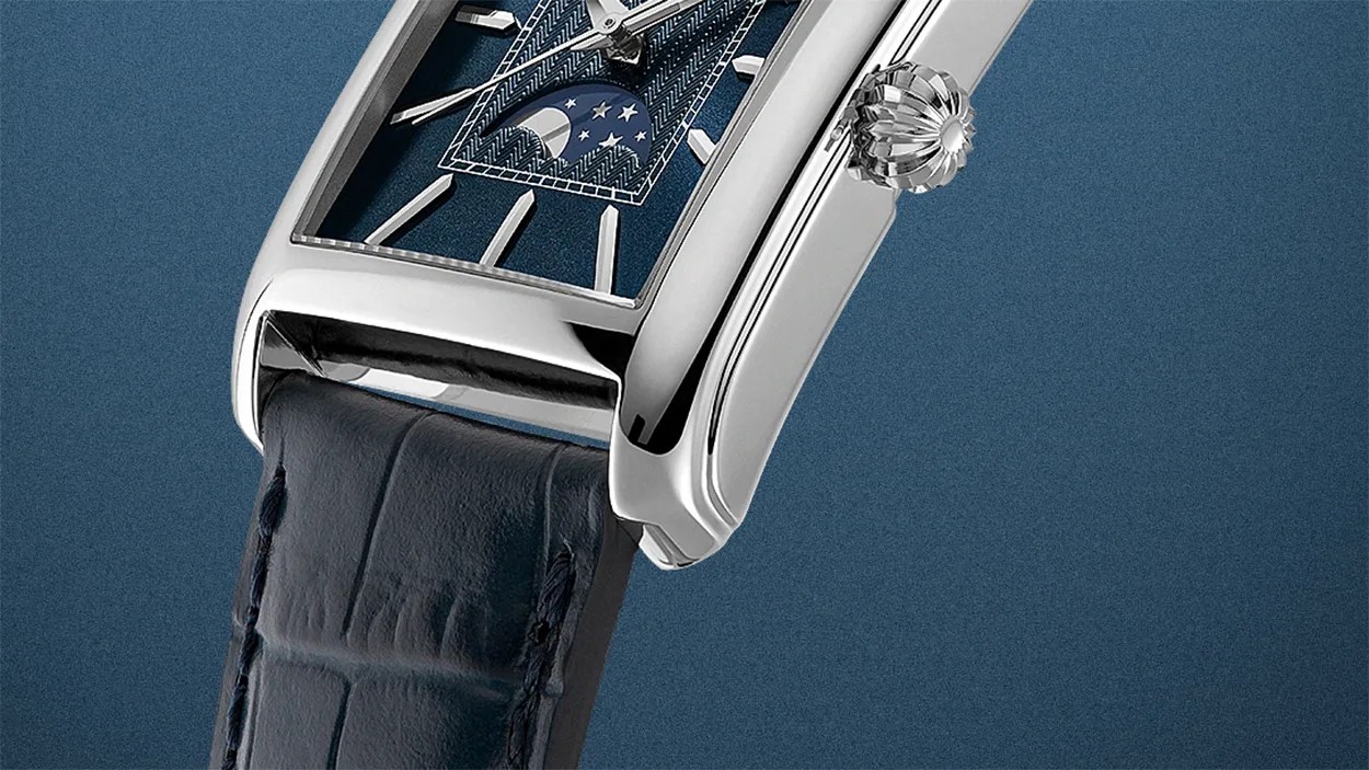 Close-up of a rectangular silver watch with a blue dial featuring a moon phase indicator and a dark blue leather strap.