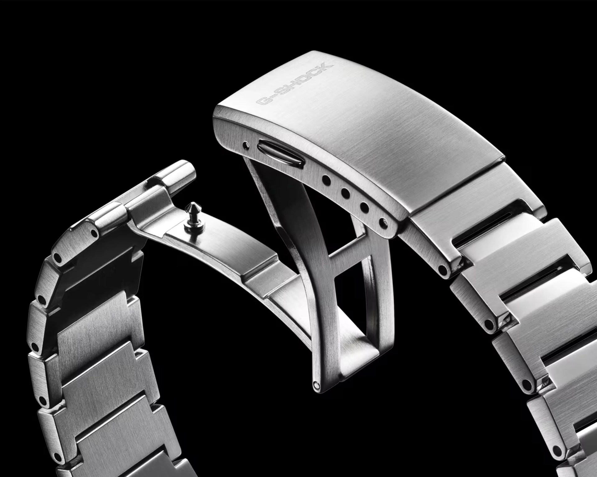 Brushed stainless steel G-Shock watch band with deployment clasp open against a black background.