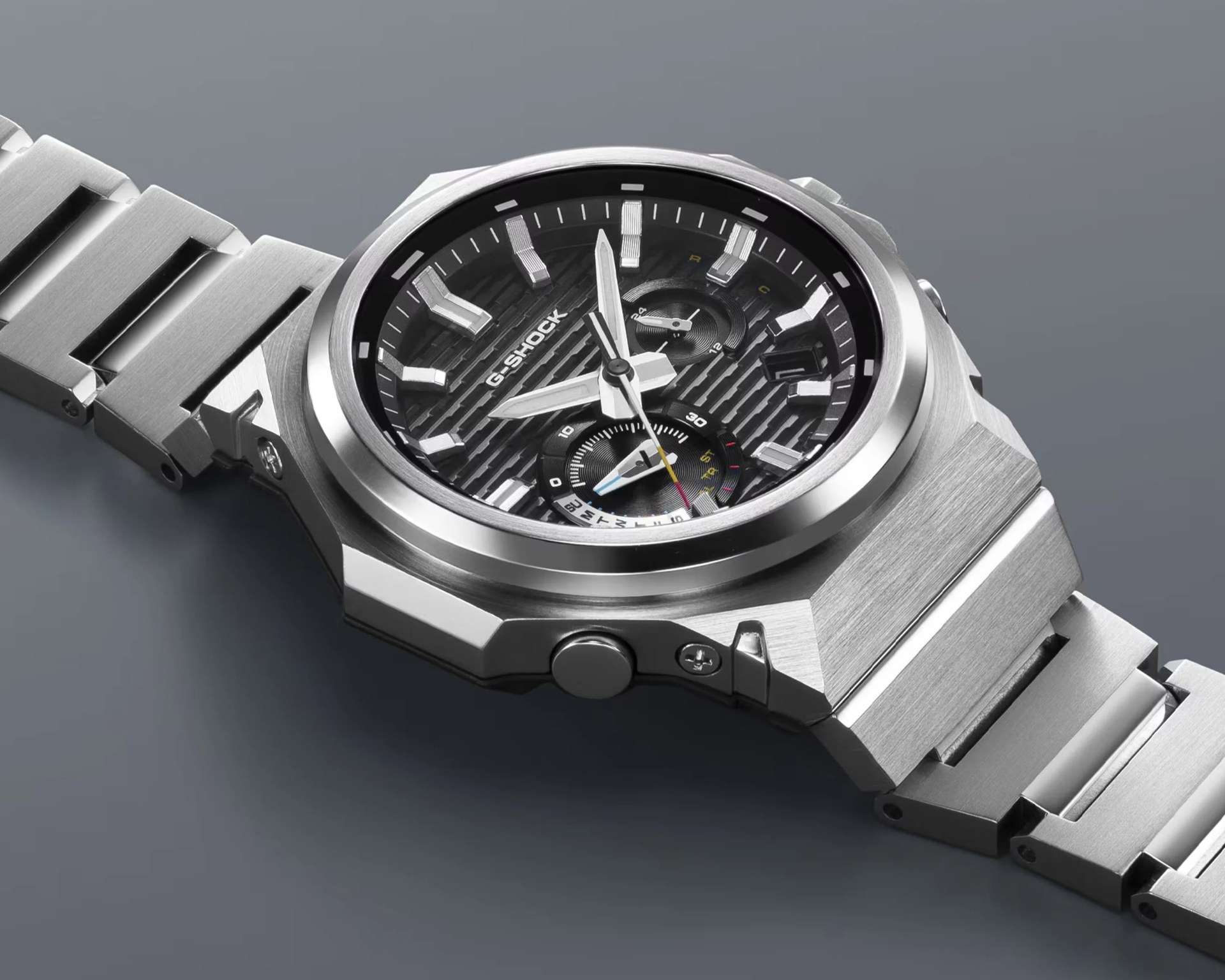 Silver stainless steel G-Shock wristwatch with black textured dial and multiple subdials on a gray surface.