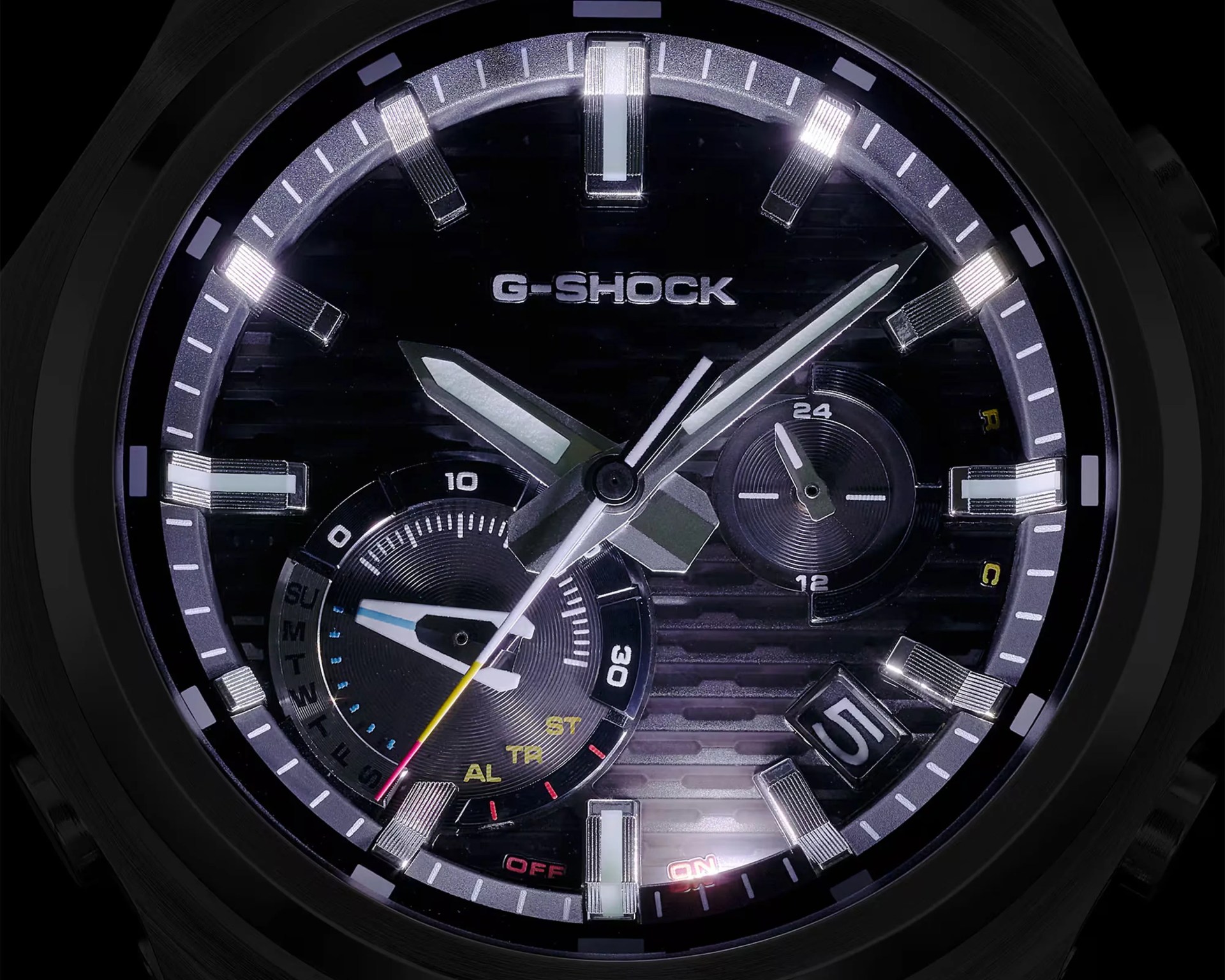Close-up of a black G-Shock watch face with silver hour markers, luminous hands, subdials, and a date window showing the number 5.