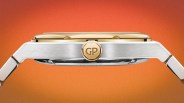Side view of a silver and gold wristwatch with a gold crown engraved with "GP" on an orange background.