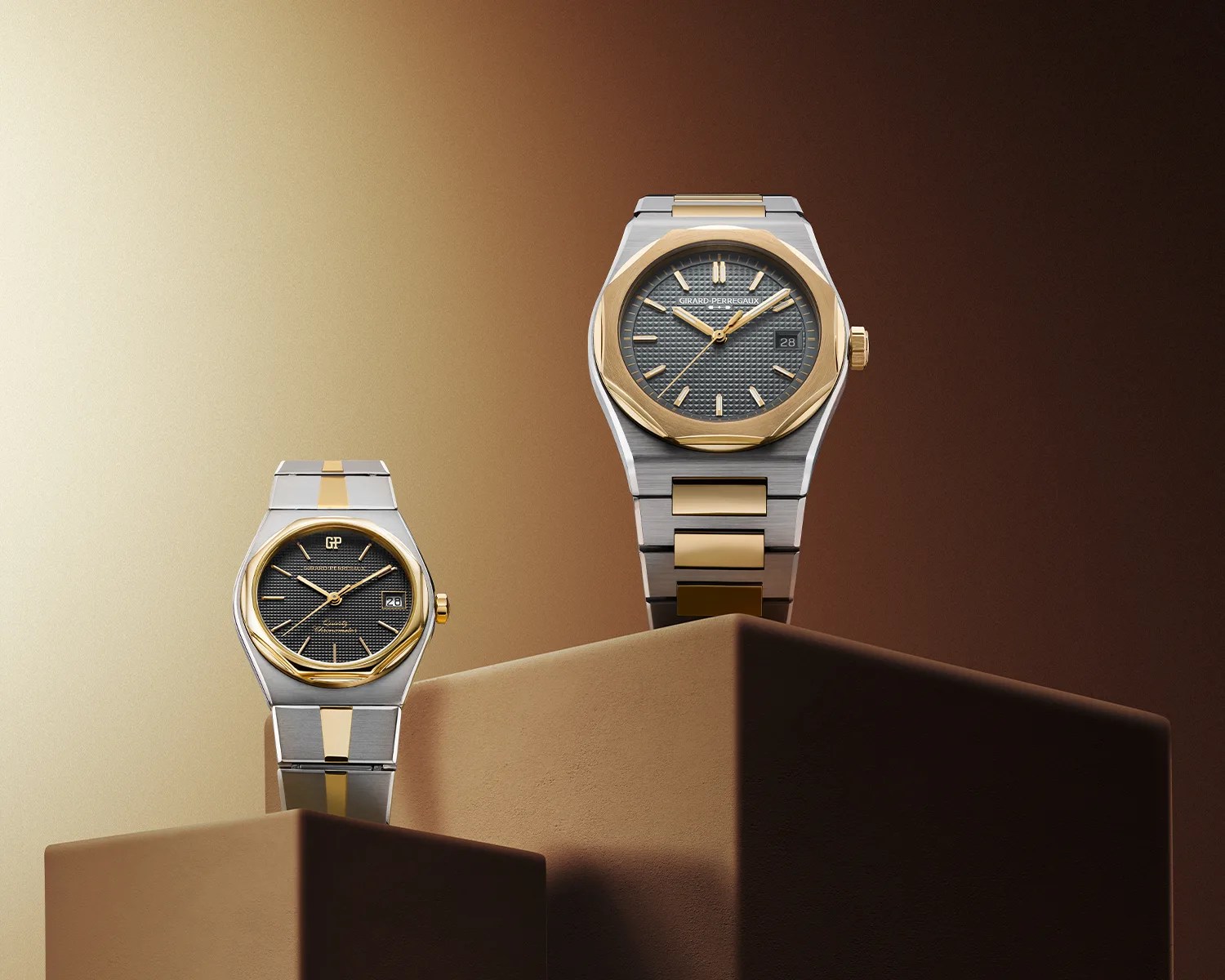 Two luxury wristwatches with gold and silver metal bands and dark textured dials displayed on brown pedestals against a gradient beige to dark brown background.