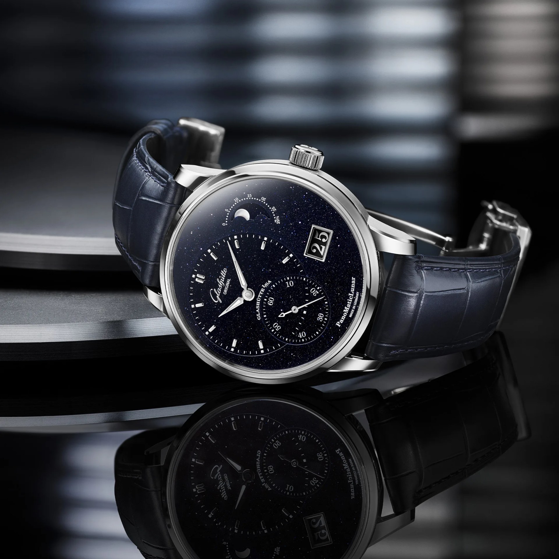 Silver wristwatch with a dark blue starry dial, moon phase indicator, date display, and blue leather strap.