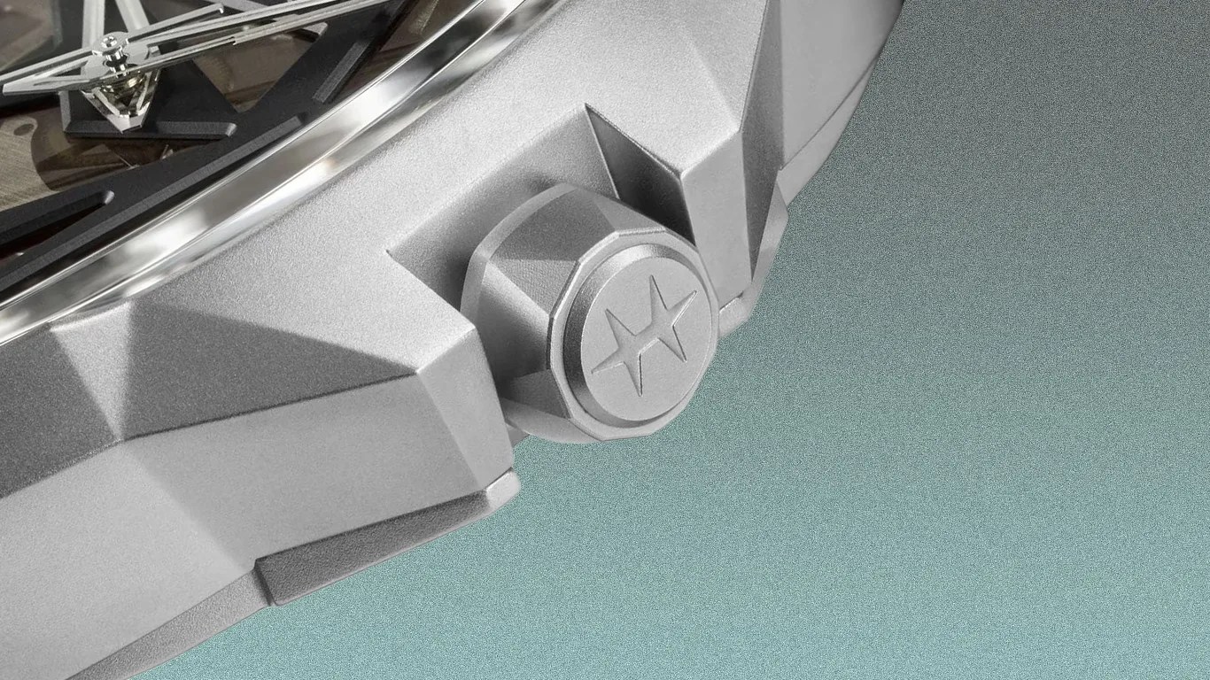 Close-up of a silver watch crown with a star emblem on a faceted metal watch case.