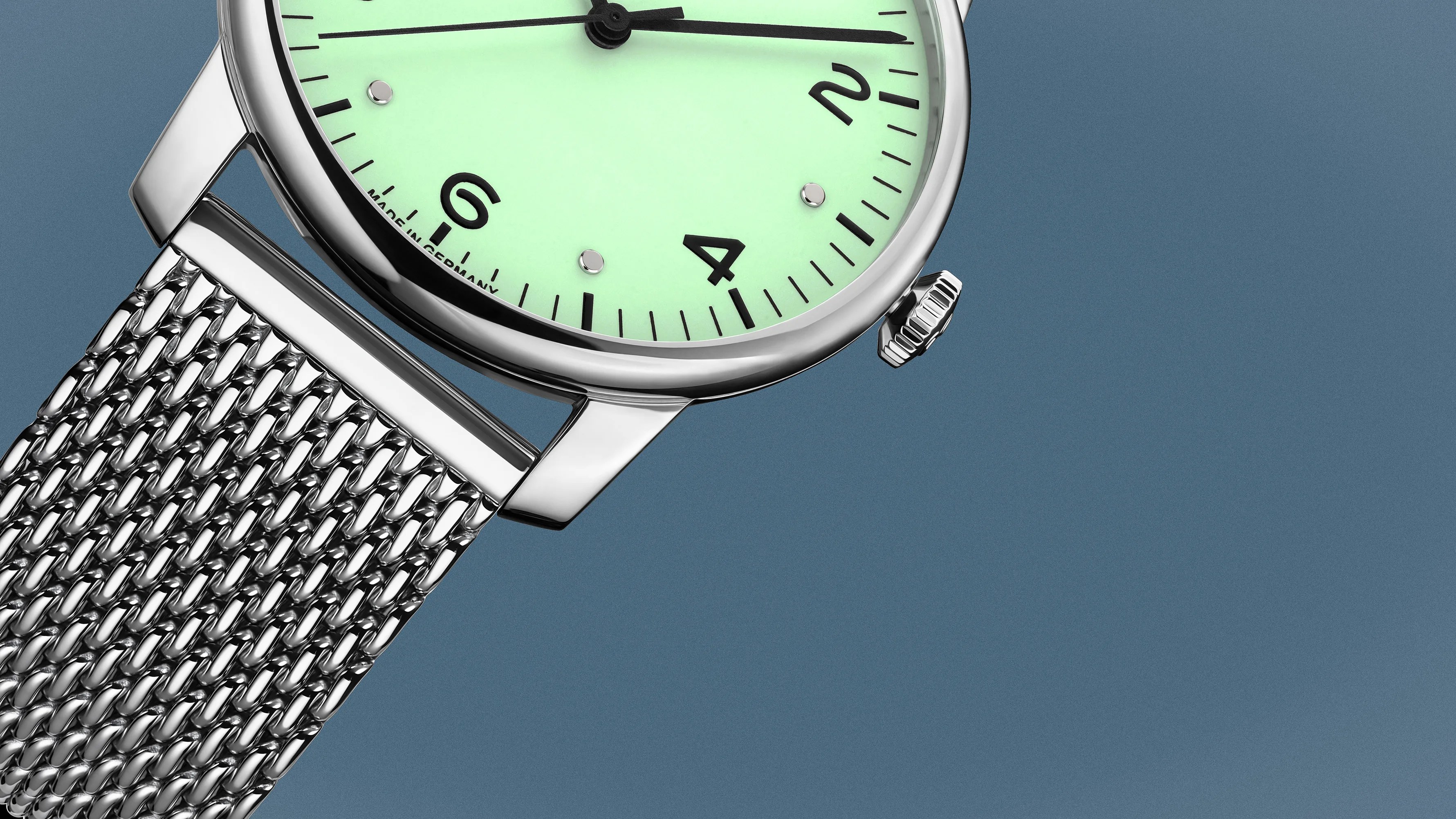 Close-up of a silver mesh watch band and a mint green watch face with black numerals and silver markers.