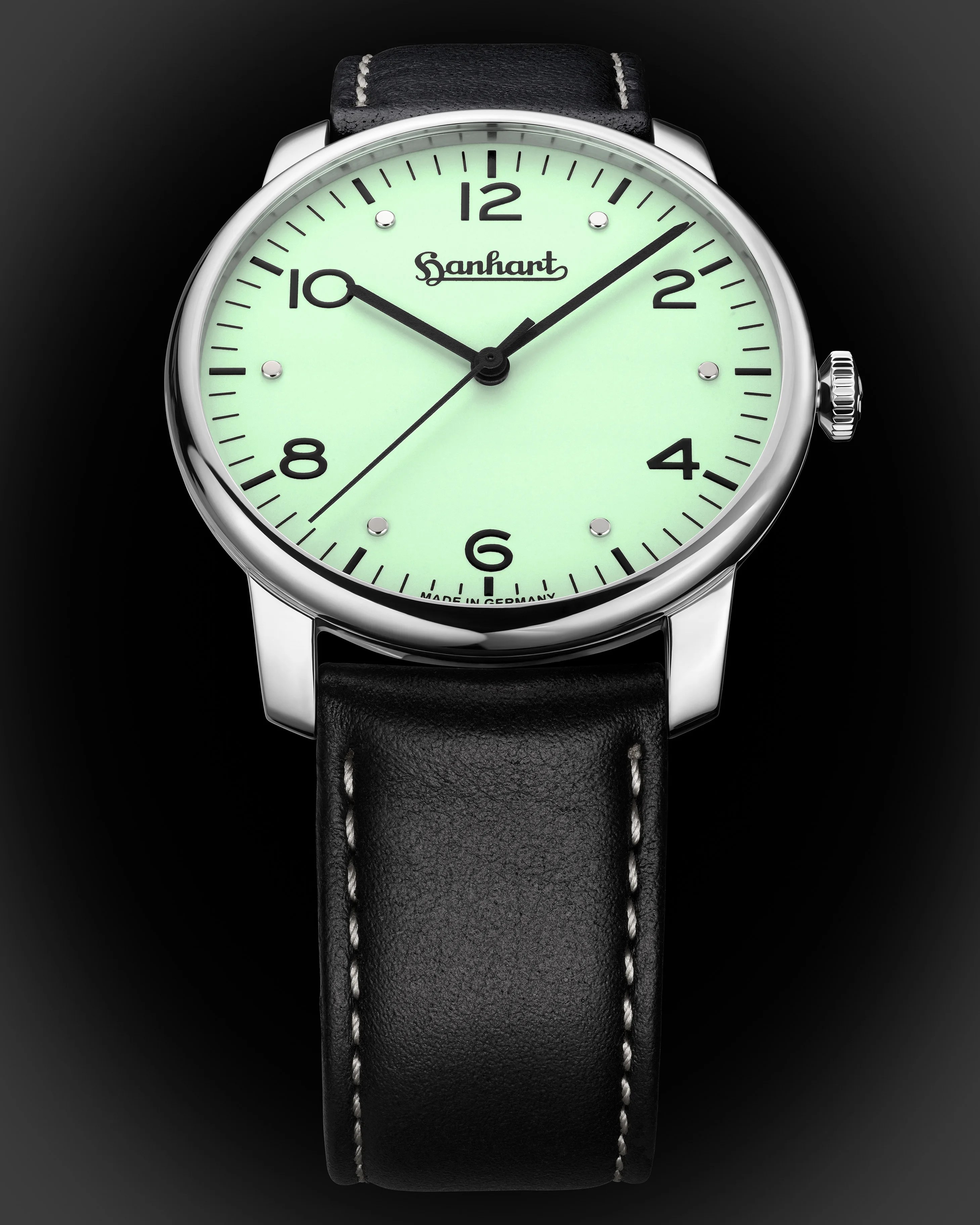 Round silver wristwatch with mint green dial, black numerals, black leather strap with white stitching.