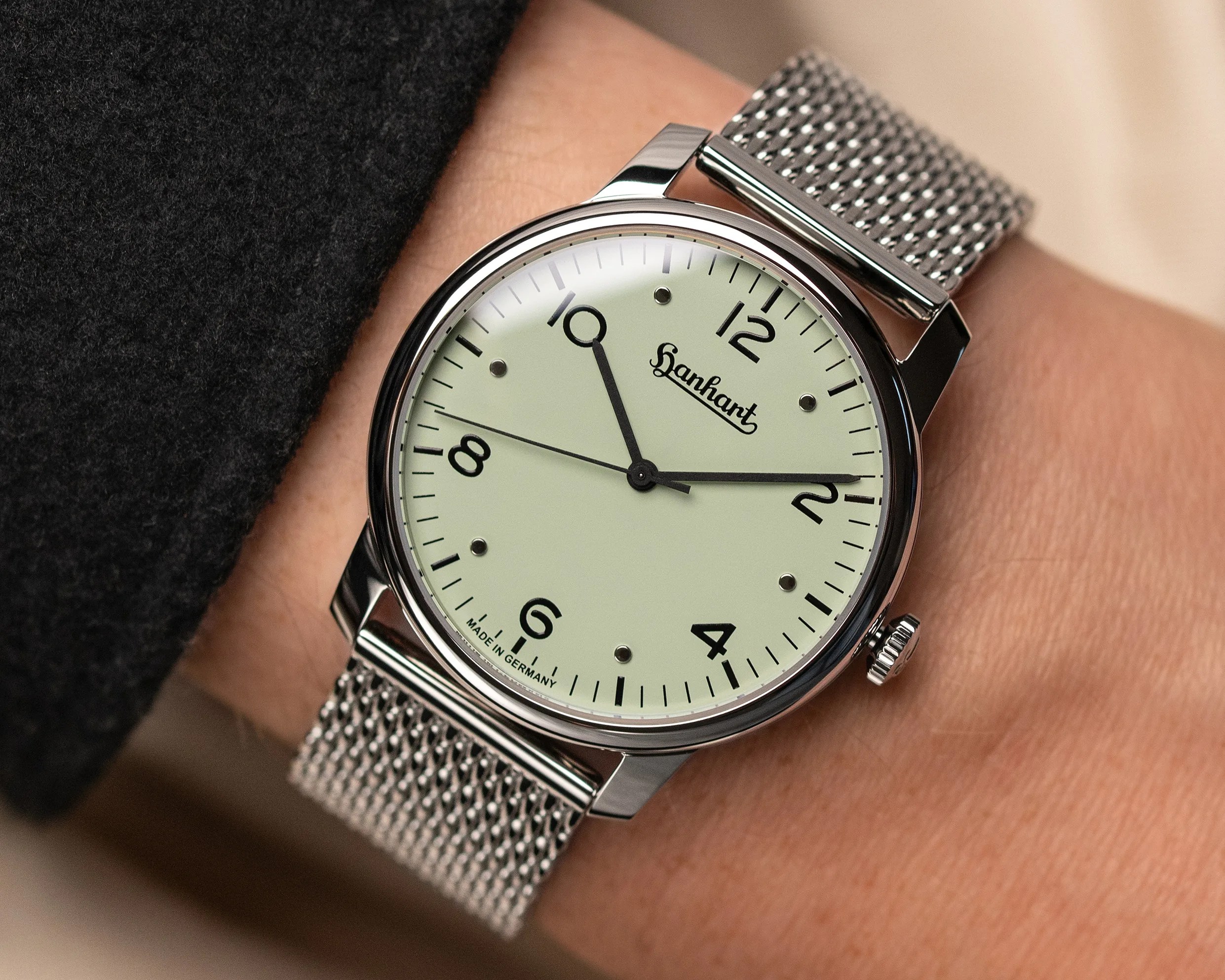 Silver mesh band wristwatch with pale green dial and black numerals showing 10:11:48.
