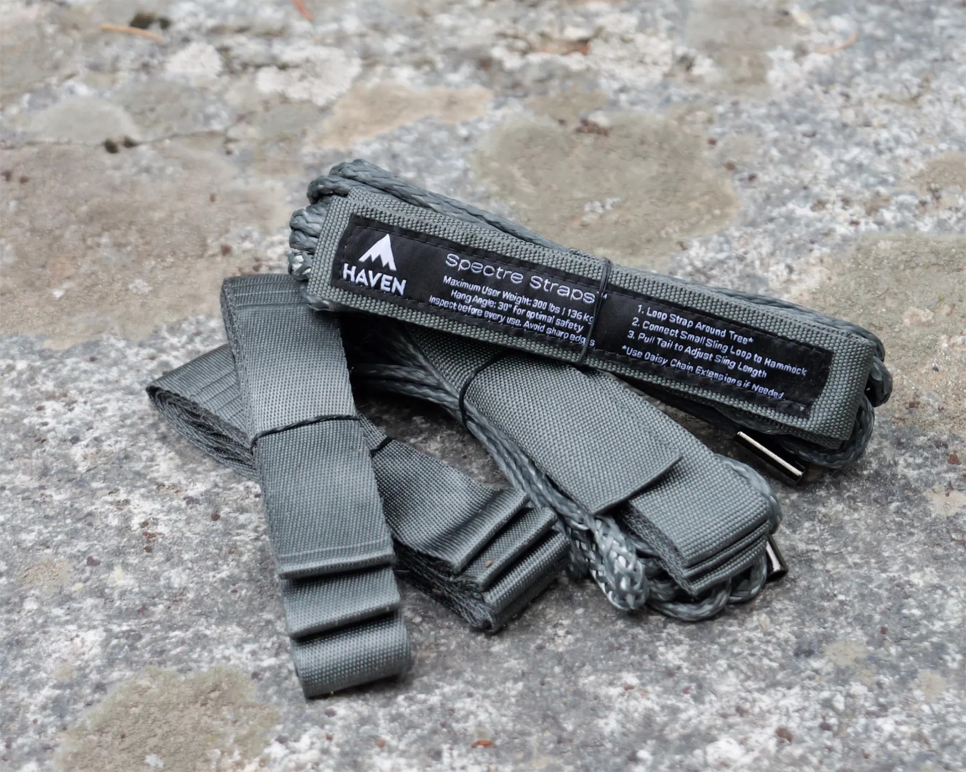 Gray woven Spectre Straps by Haven with black label and metal loops on a stone surface.