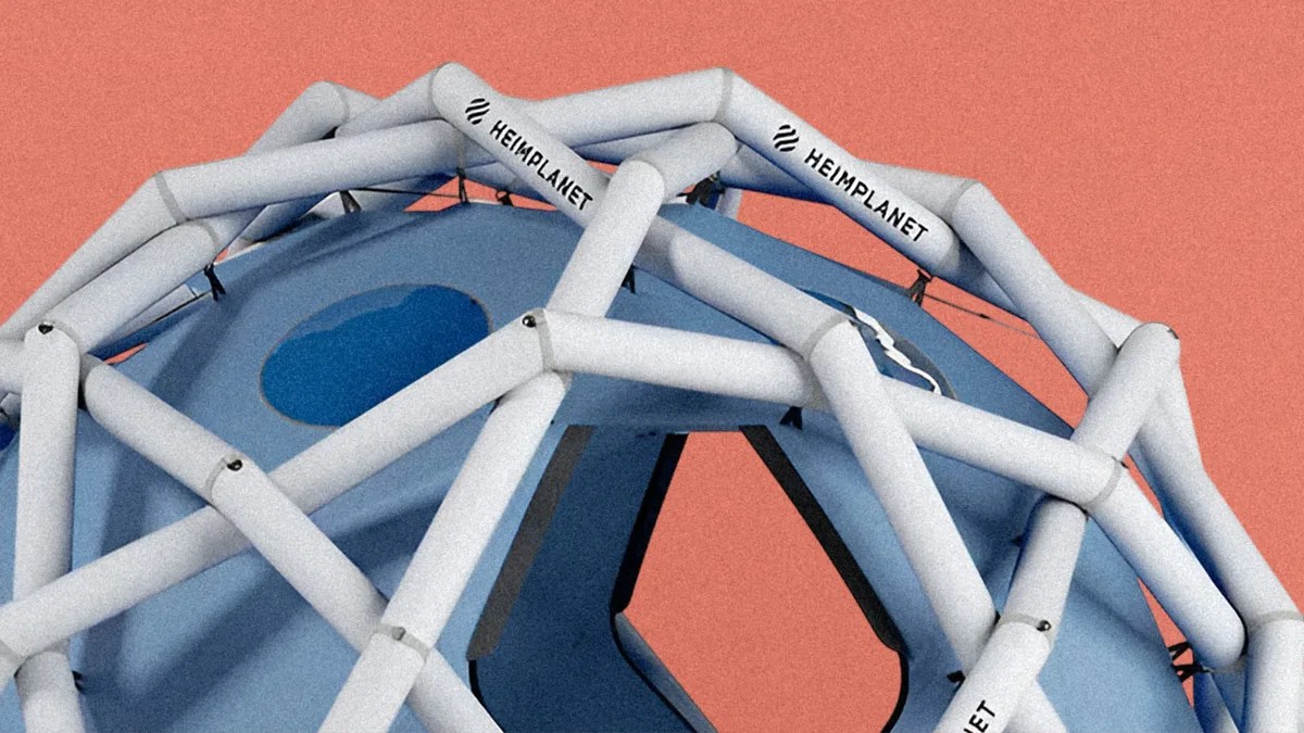 Close-up of a blue geodesic dome tent with white inflatable frame tubes labeled "HEIMPLANET" against a coral background.